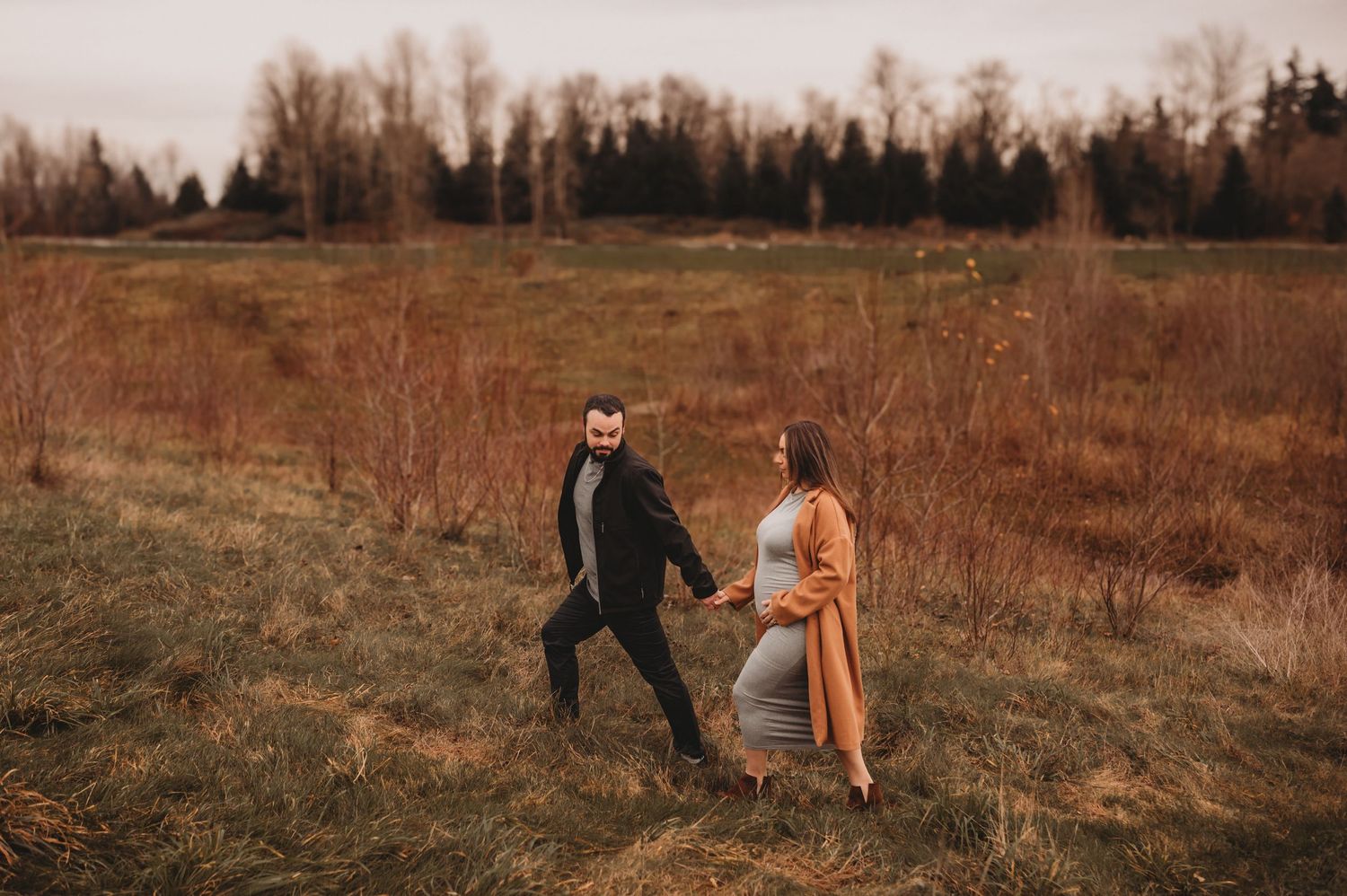 Couple playfully walking through autumn meadow during maternity shoot.