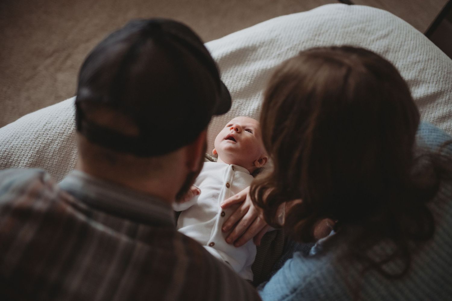 Two parents gazing lovingly at their newborn baby lying on a soft blanket.