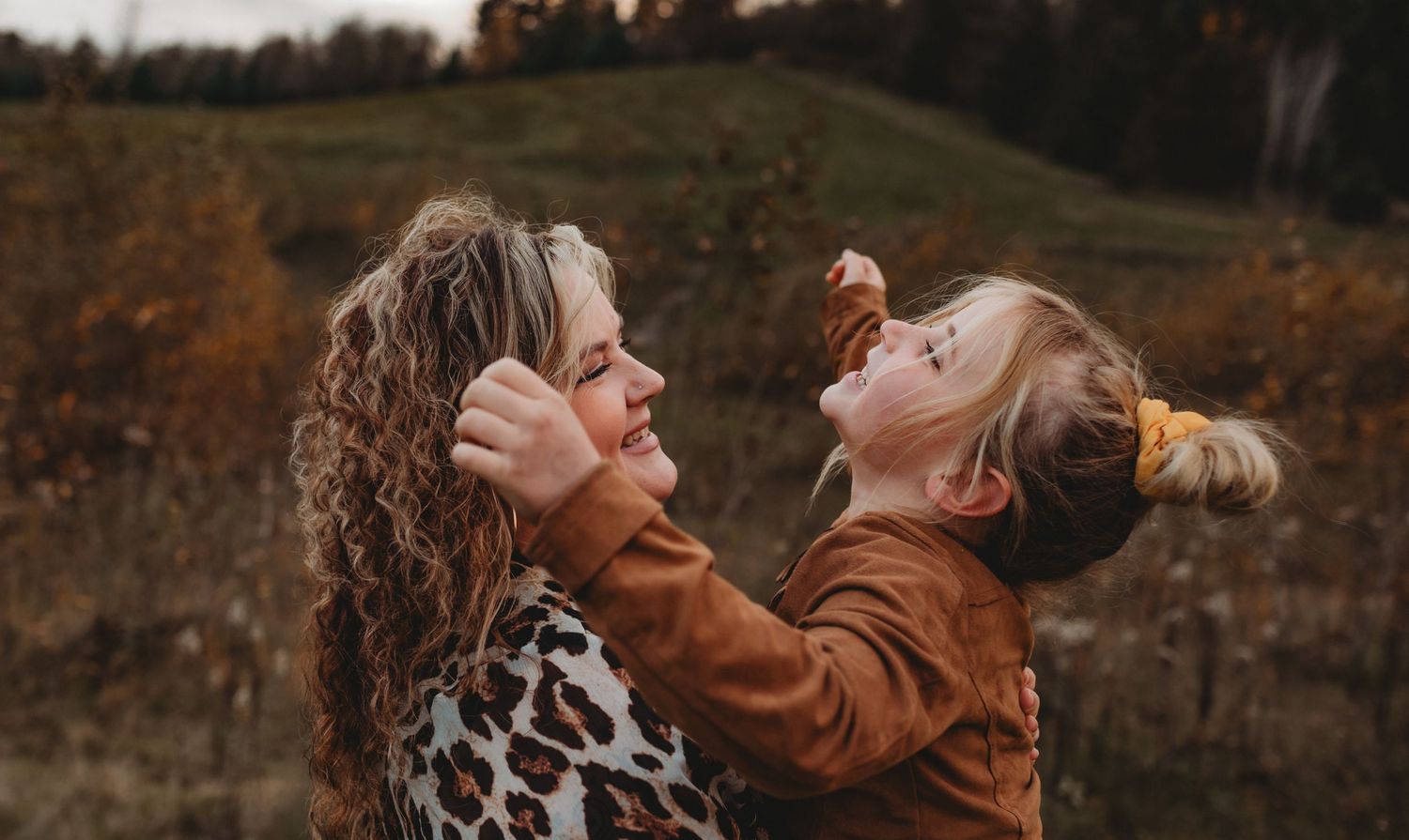 Woman and young girl laughing together in an autumn field, sharing a joyful moment outdoors.