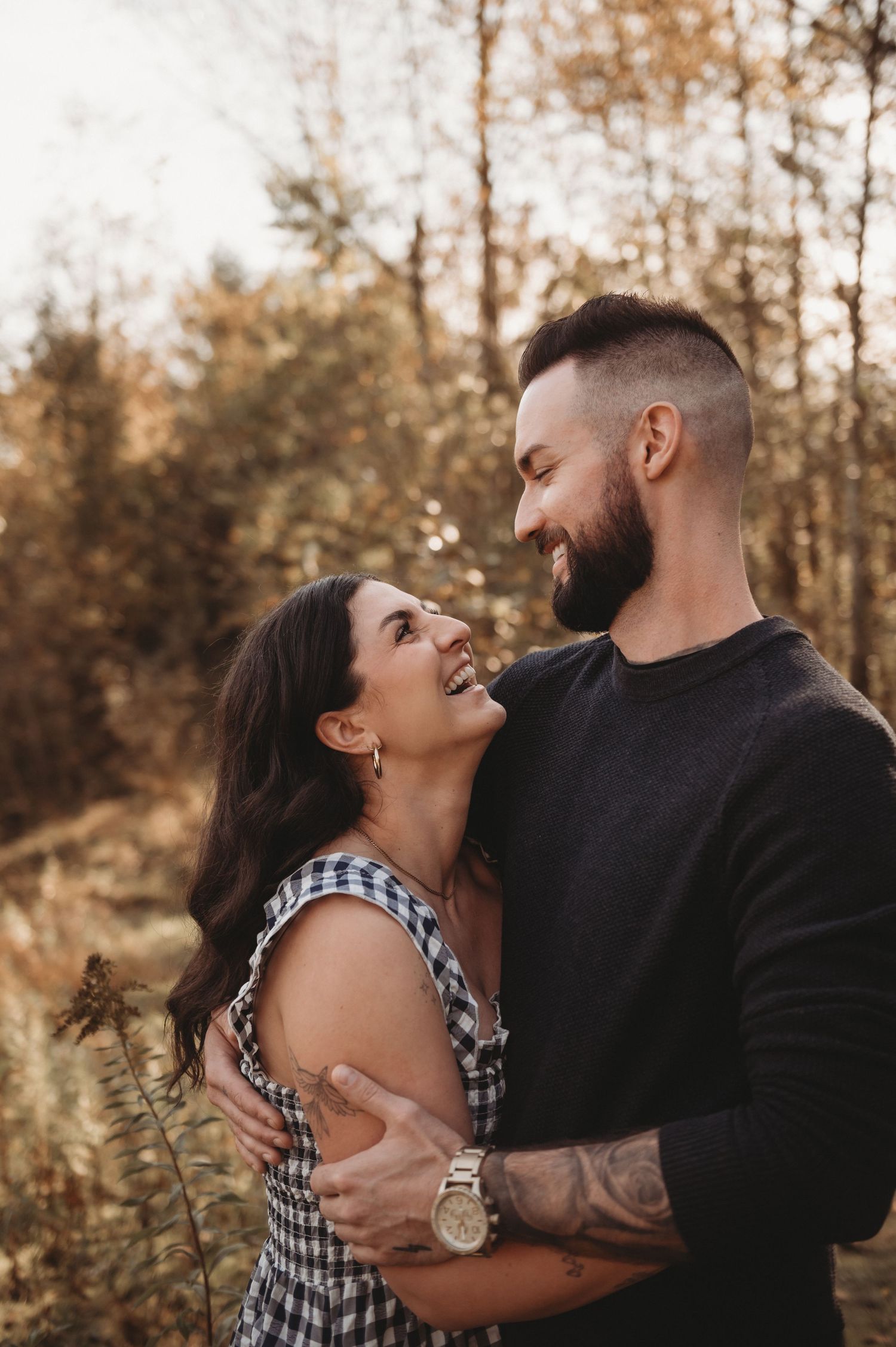 A joyful couple laughs and embraces outdoors surrounded by warm autumn foliage.