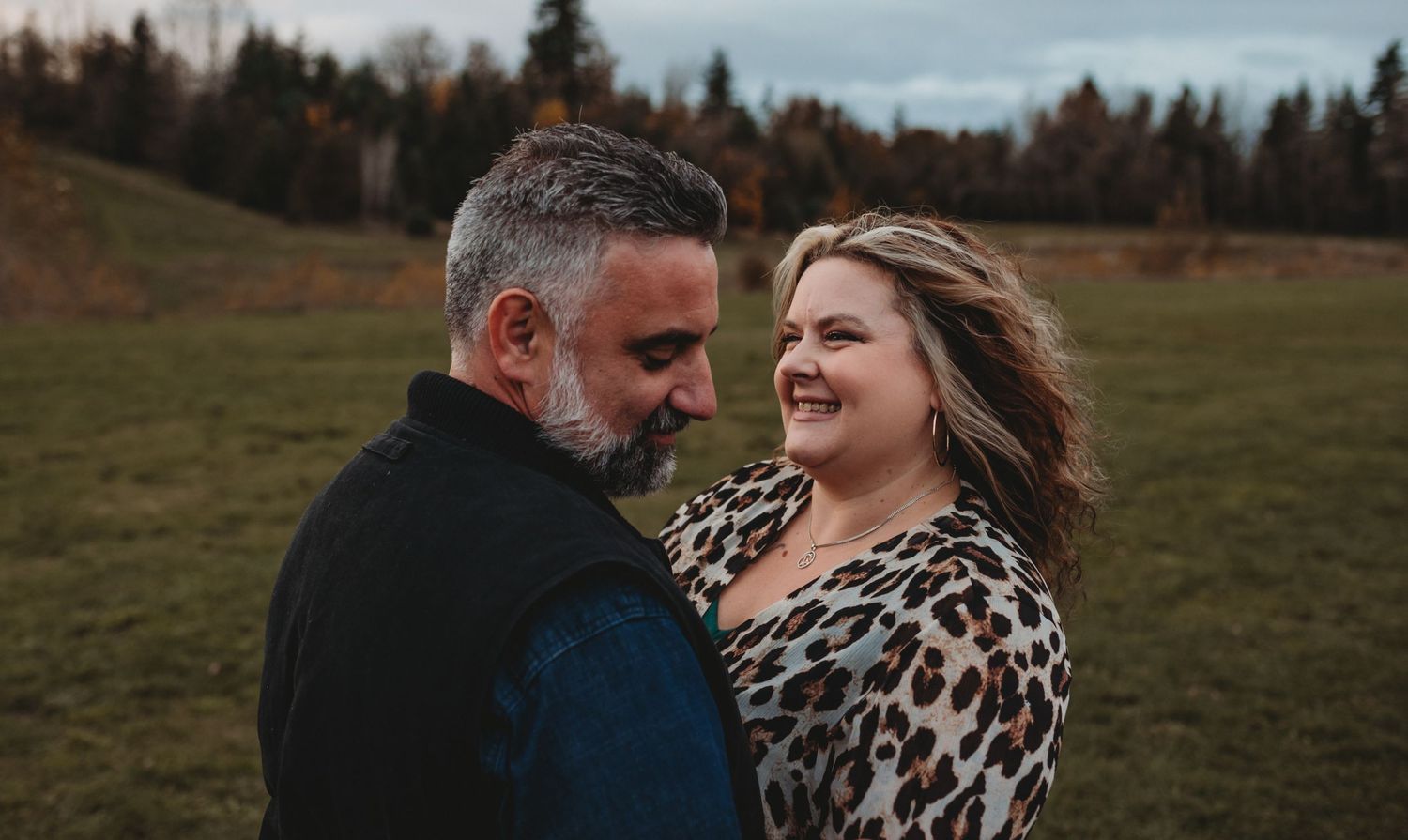Smiling couple in a green field during autumn, woman wearing leopard print top.