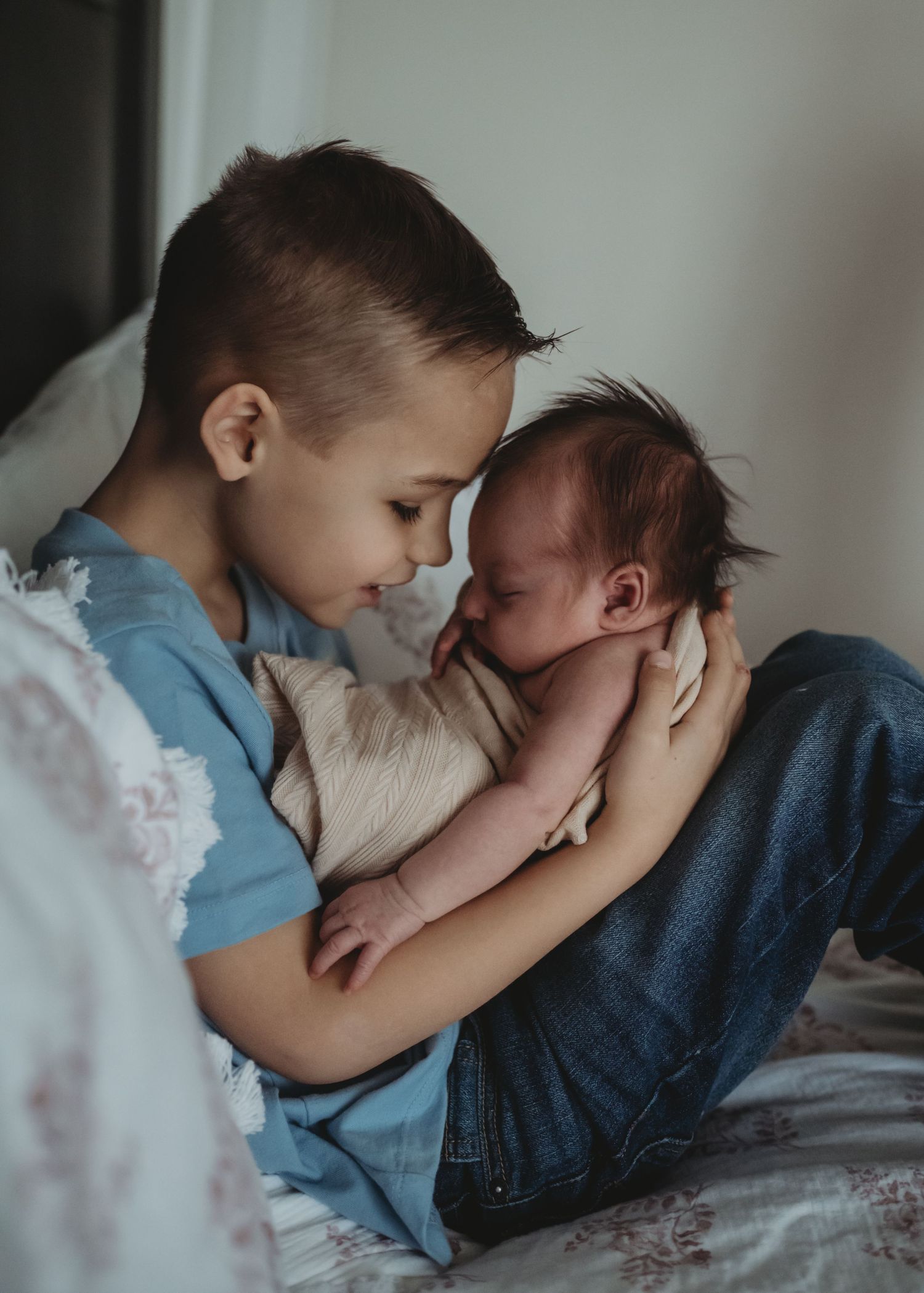 Young boy tenderly holding and bonding with newborn baby sibling on a bed, family photography.