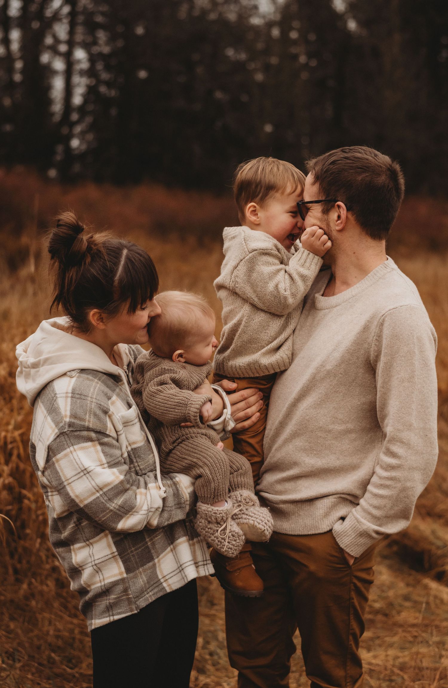 Family of four with two toddlers sharing playful moment in golden autumn field outdoors.