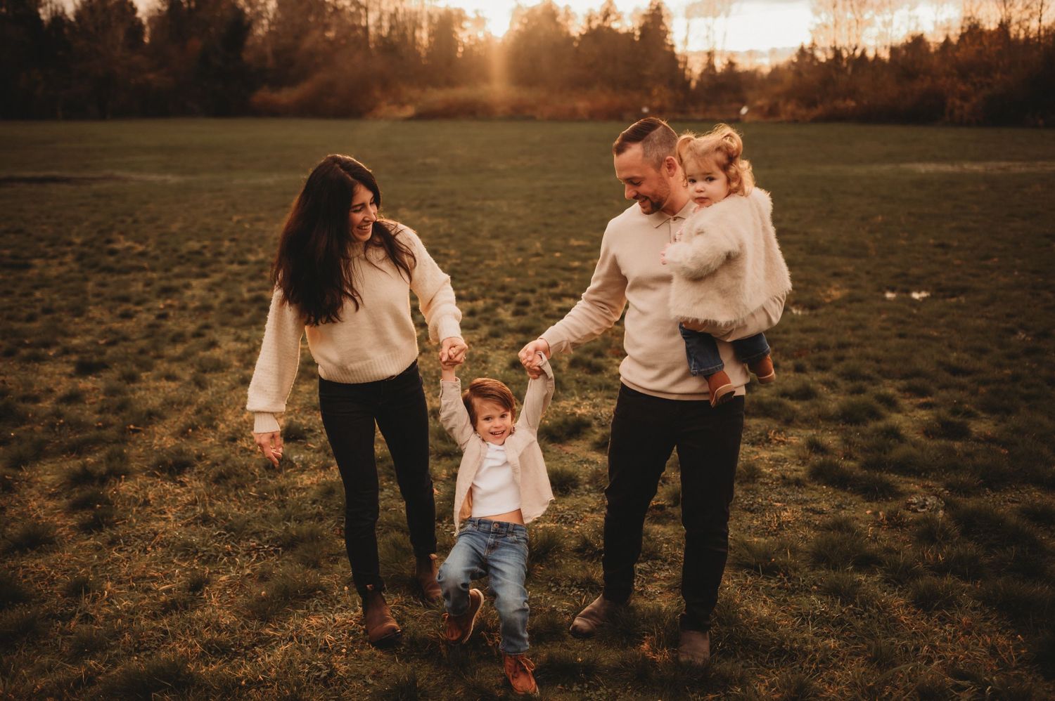 Parents and two young children walking together in a warm sunset field.