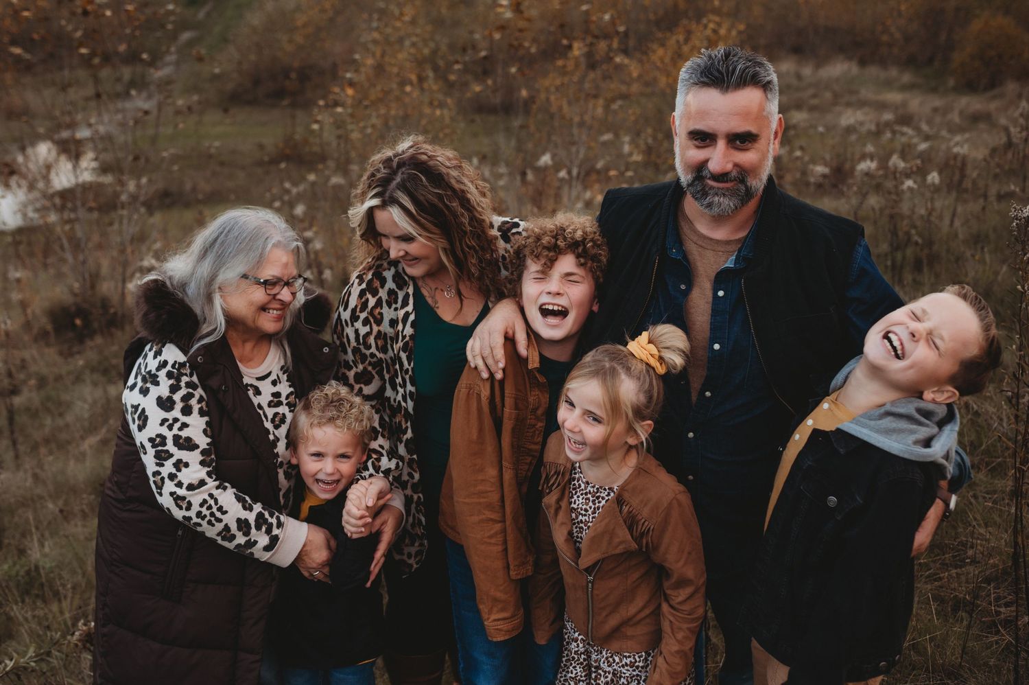A joyful multigenerational family laughs together in an autumn field during an outdoor portrait.