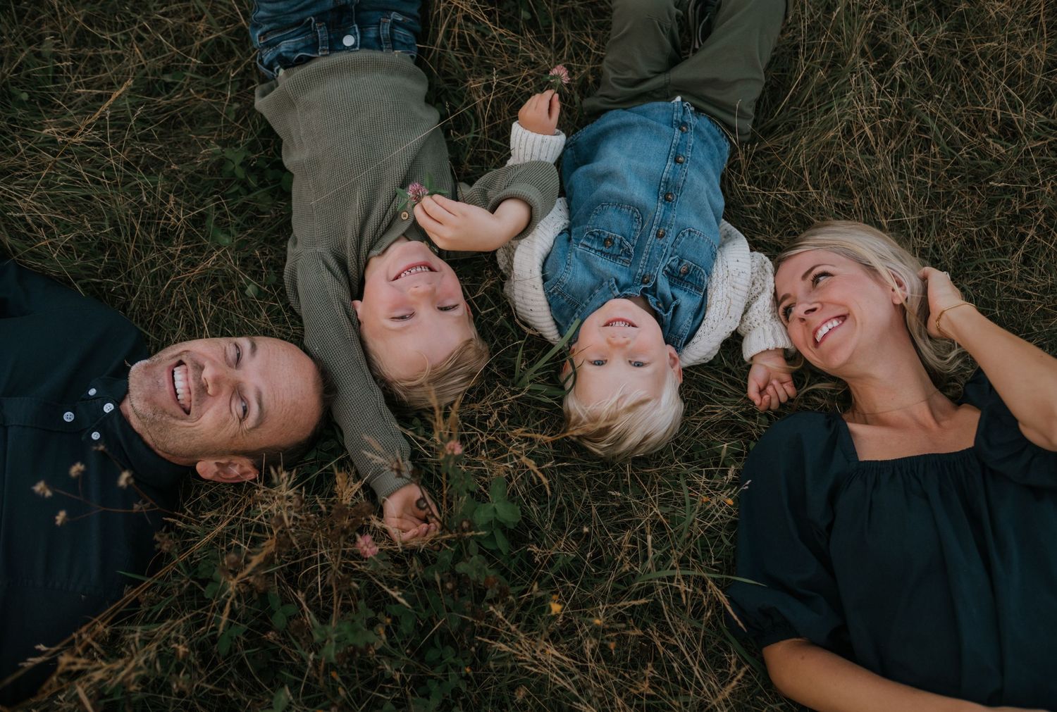 Happy family of four lying on grass laughing together in overhead autumn portrait.