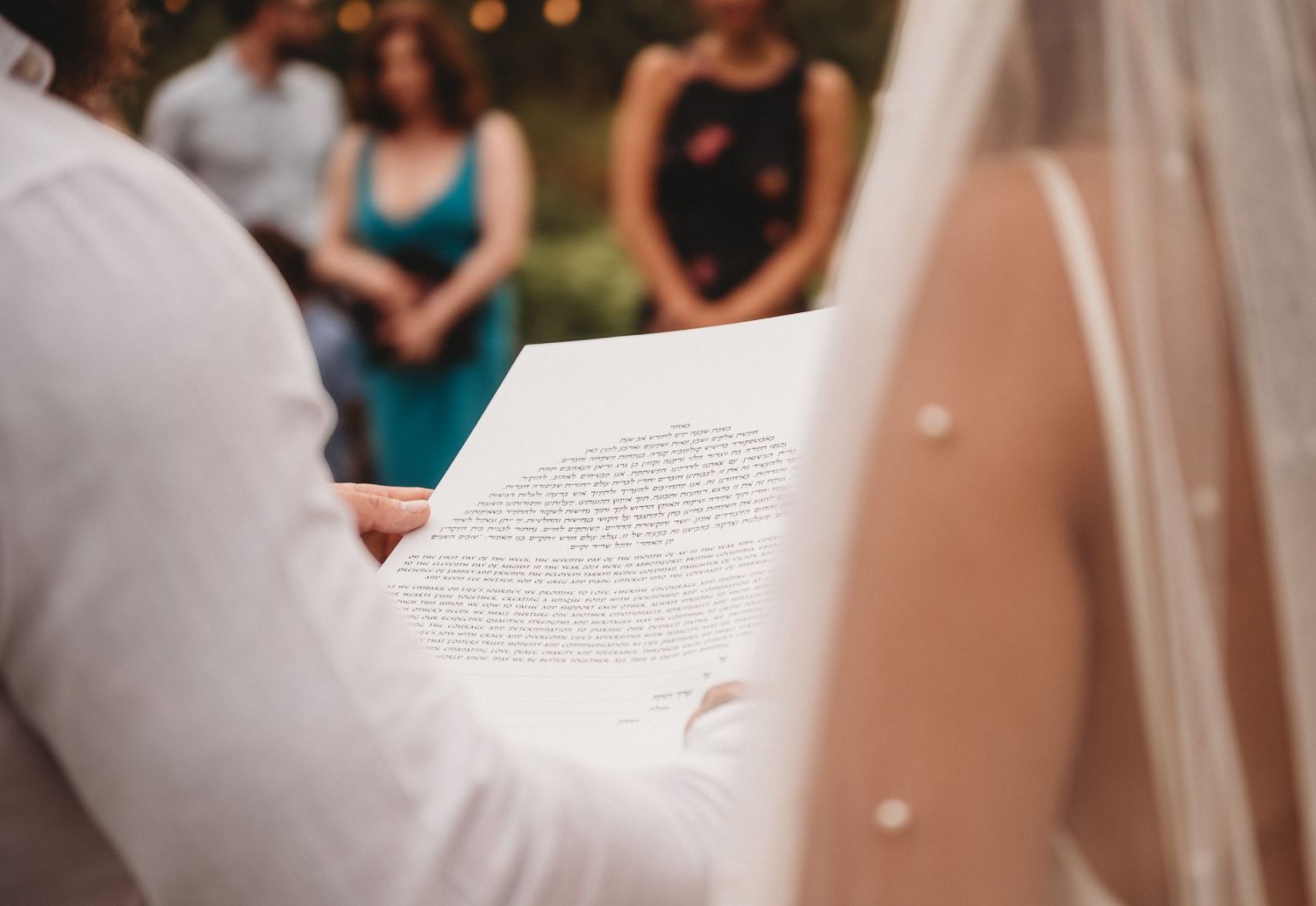 Groom reading heartfelt vows from paper during outdoor wedding ceremony with guests watching.