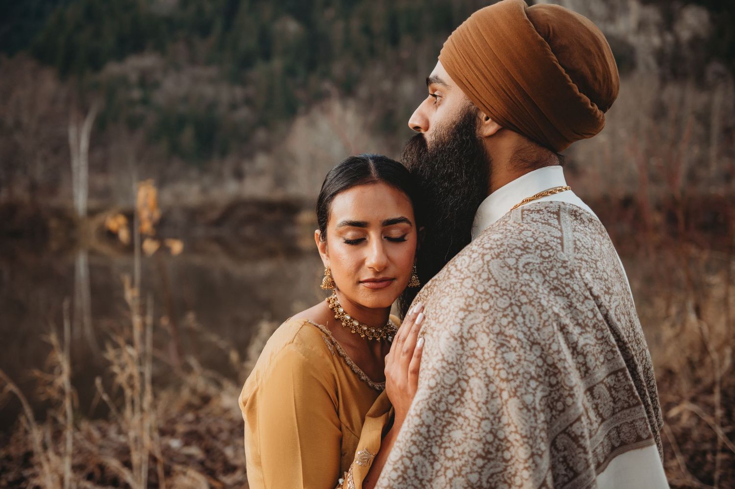 Sikh bride in mustard yellow lehenga resting her head on groom's chest in a serene outdoor setting.