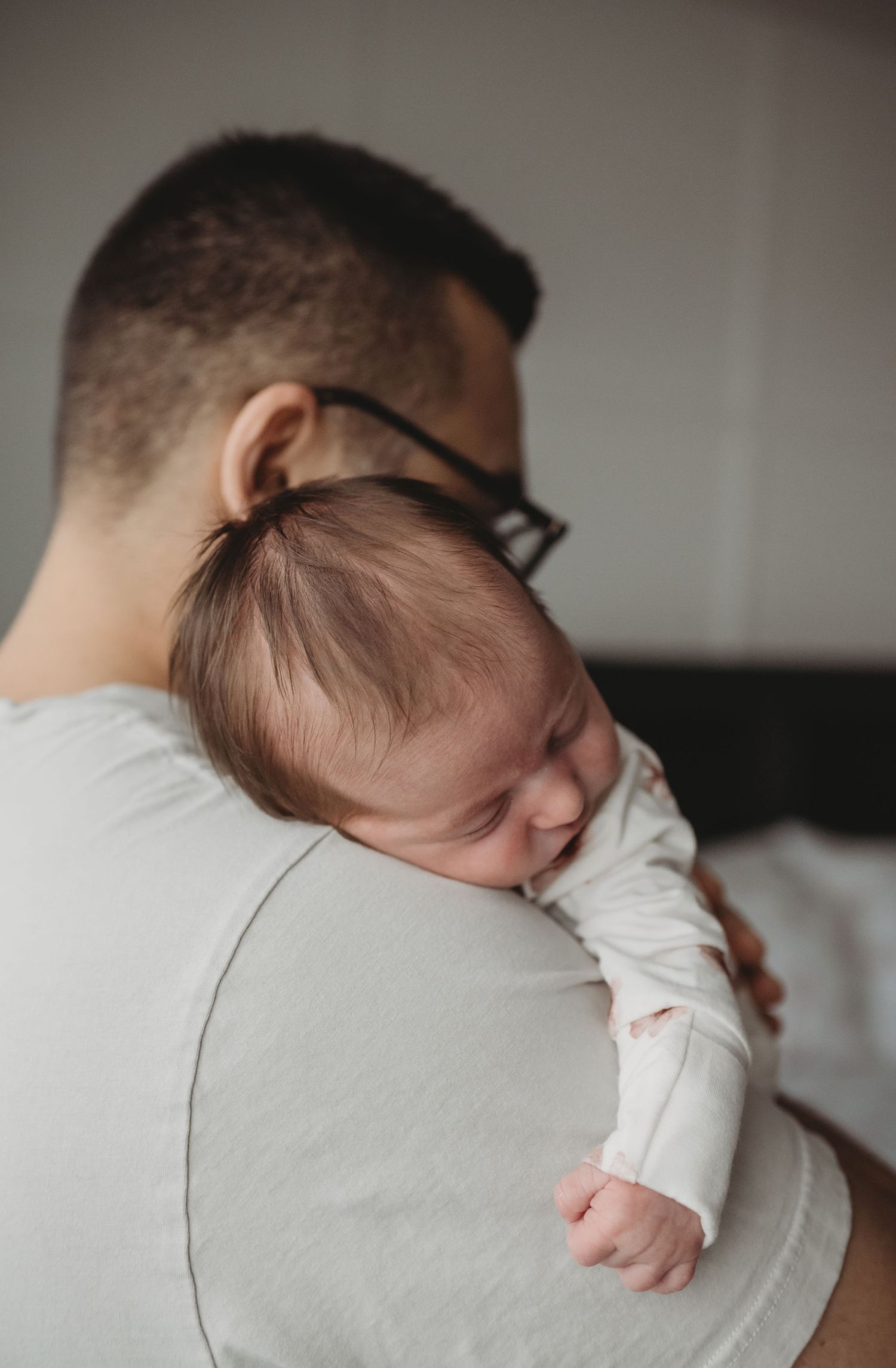 A father holds a peacefully sleeping newborn baby against his shoulder in a cozy room.