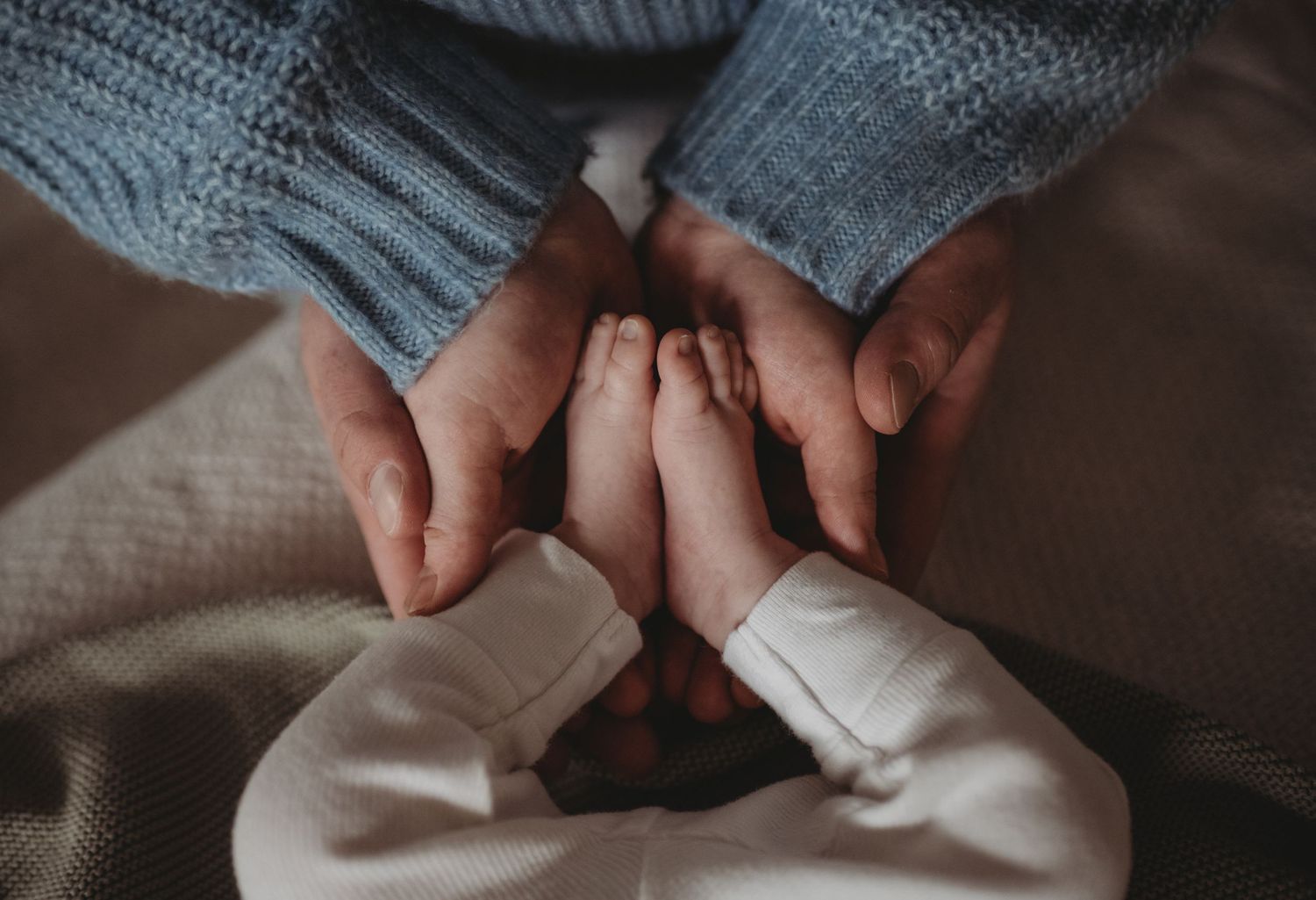 Two parents hands gently holding newborn baby feet together, close-up newborn photography.