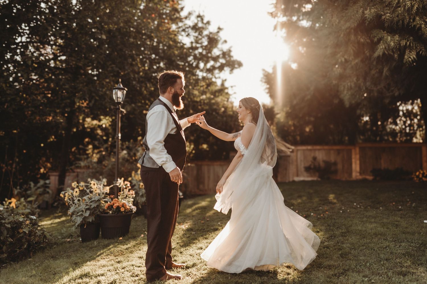 A bearded groom twirls his bride in a flowing white gown in a sunlit garden during wedding portraits.