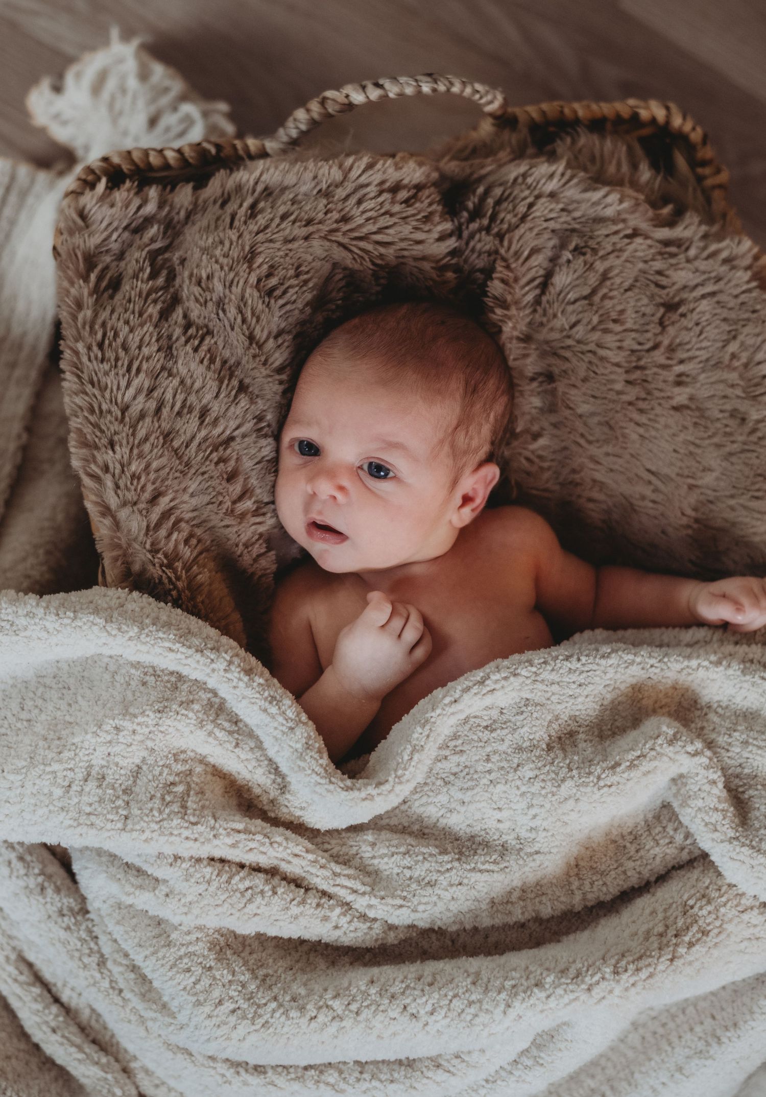 Peaceful newborn baby lying in a wicker basket lined with a fluffy brown blanket.