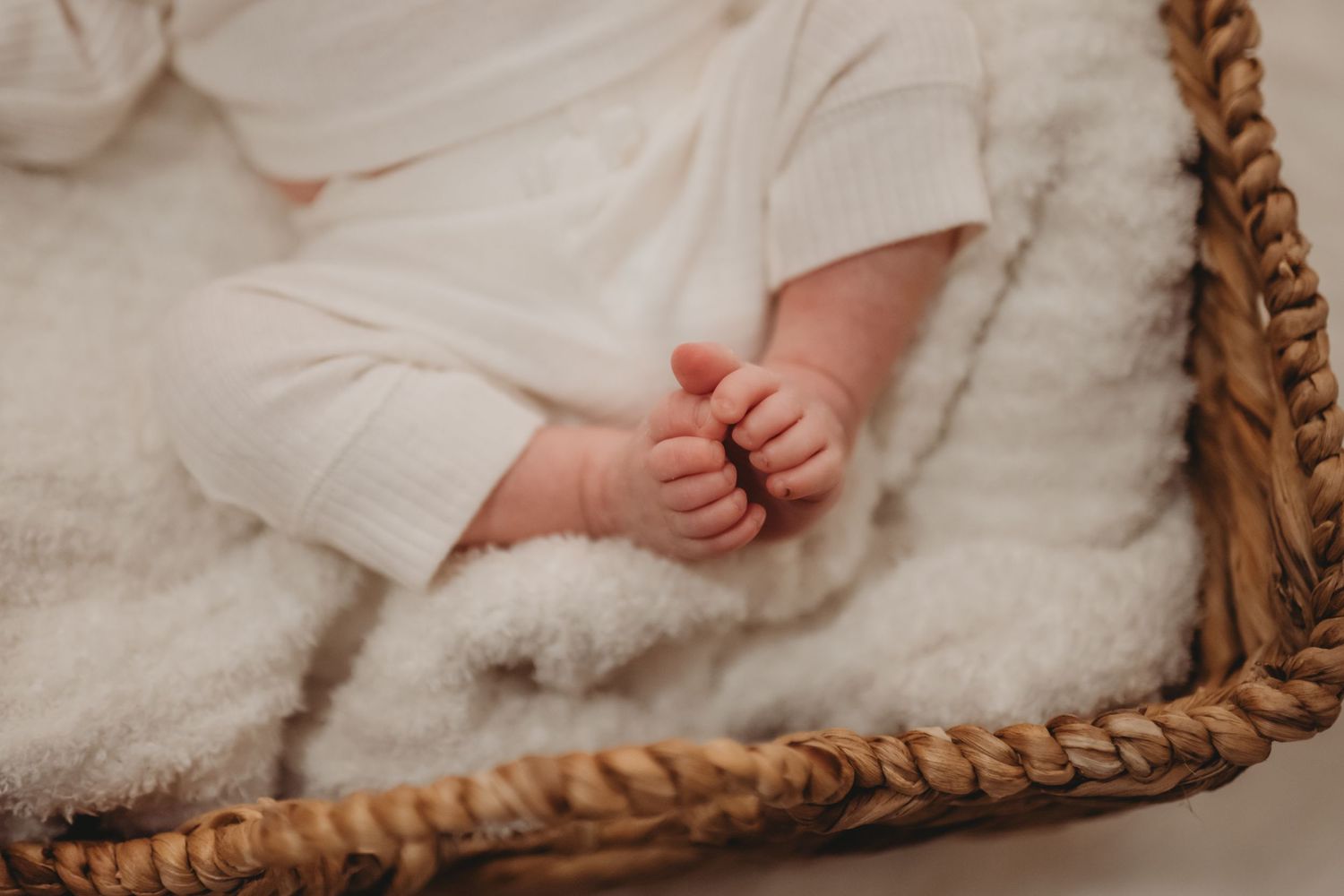 A newborn baby\u2019s tiny feet rest on a soft white blanket inside a woven basket.