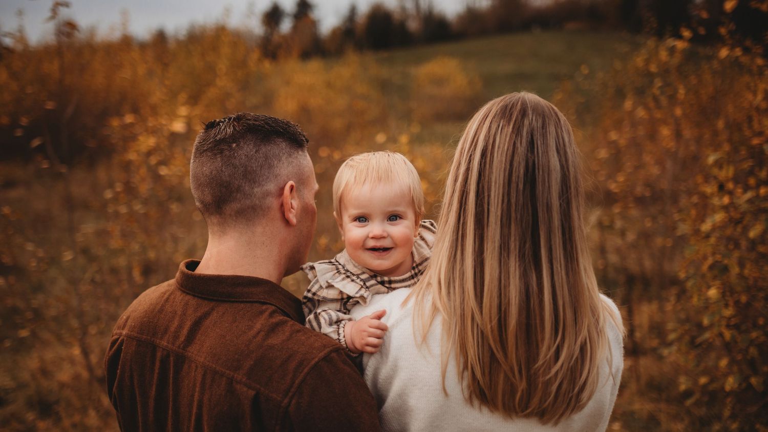 Young family with baby enjoying golden autumn field during outdoor fall family photography session.