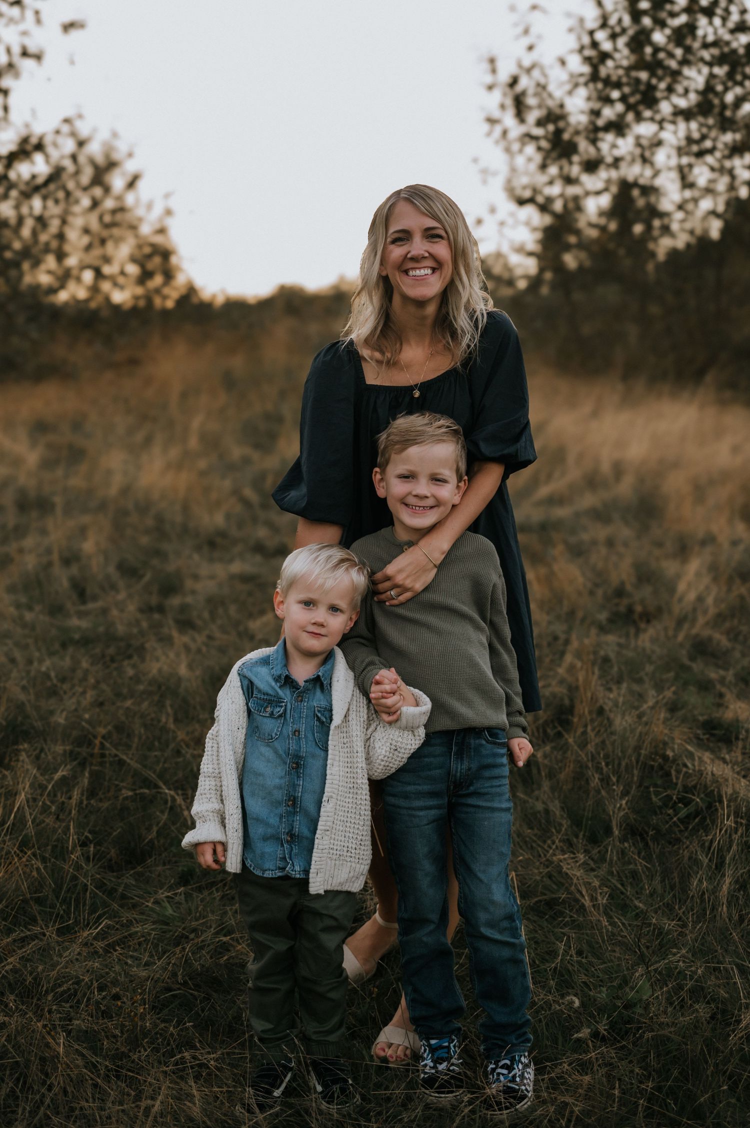 Smiling mother standing with her two young sons in a golden autumn field at sunset.