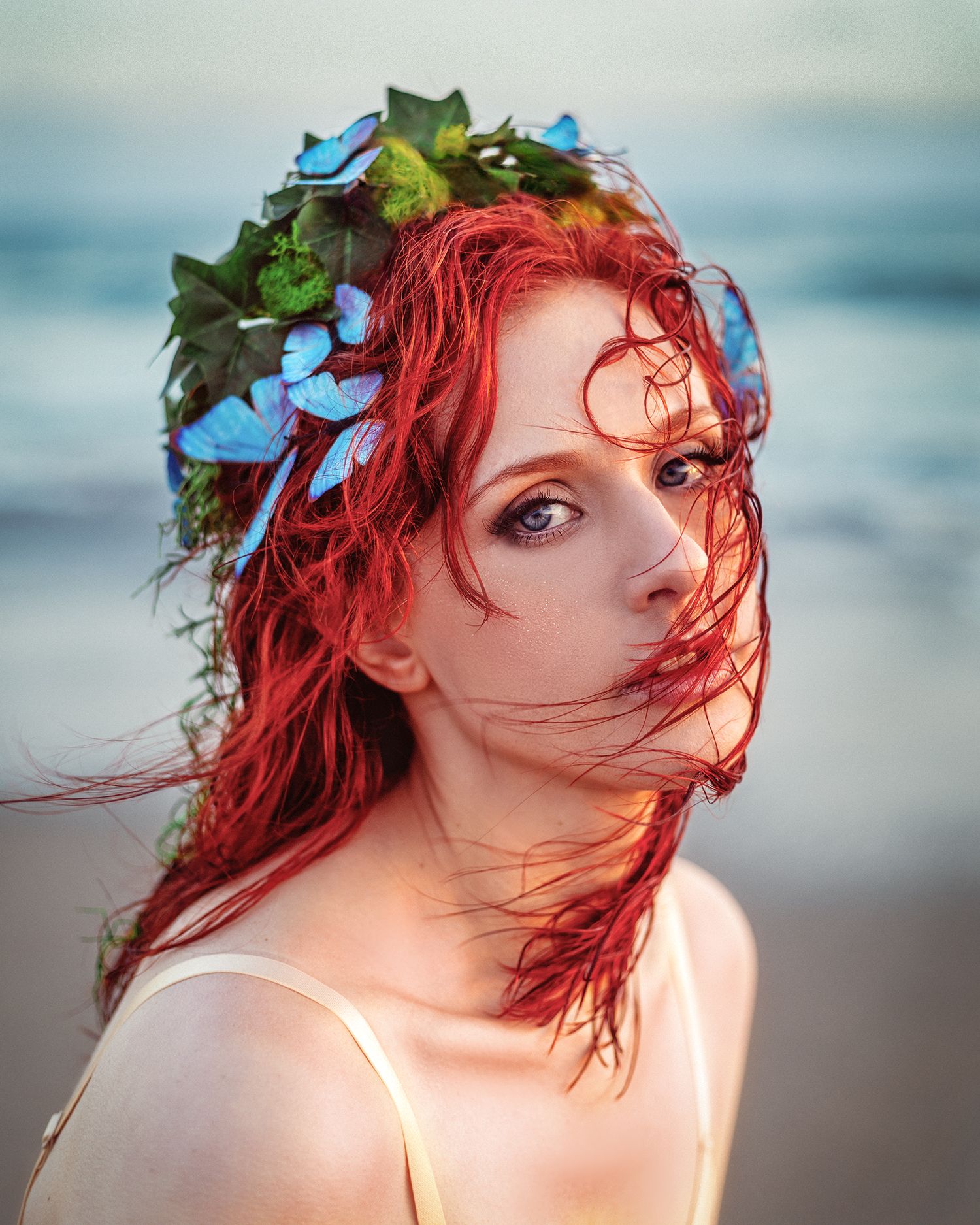 Cinematic fine art portrait of female model at Malibu Beach at golden hour, looking into the camera as a sea siren, with blue butterflies.
