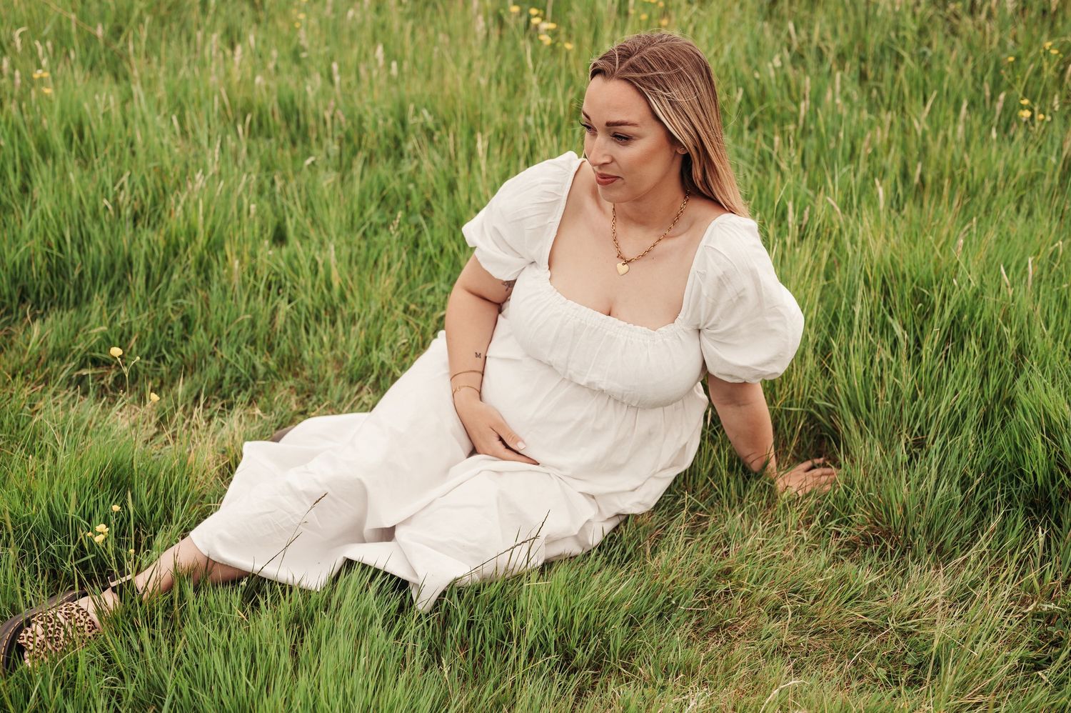 A person in a white puff-sleeve dress reclines in a grassy meadow during golden hour.