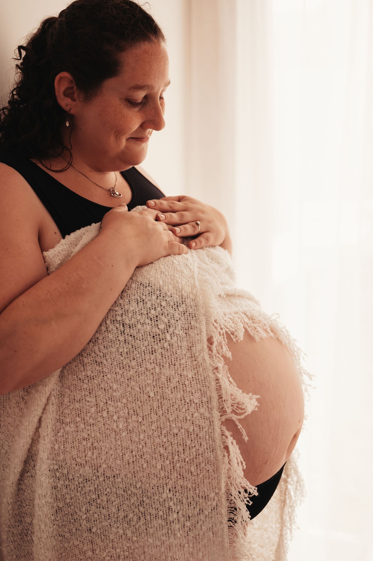 Intimate maternity portrait with cream lace wrap and black top in natural window light.