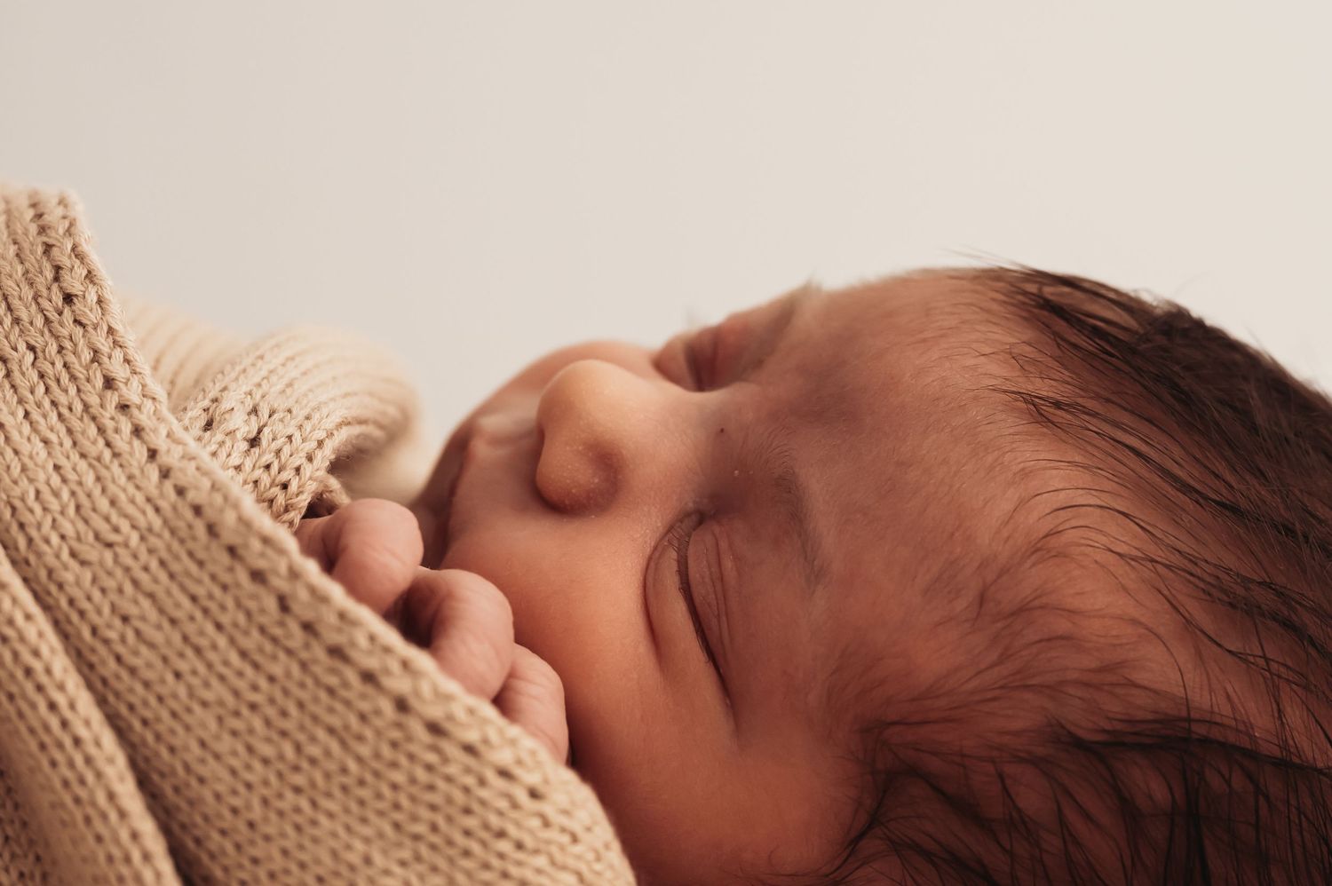 Sleeping baby with dark hair swaddled in cream colored knit wrap.
