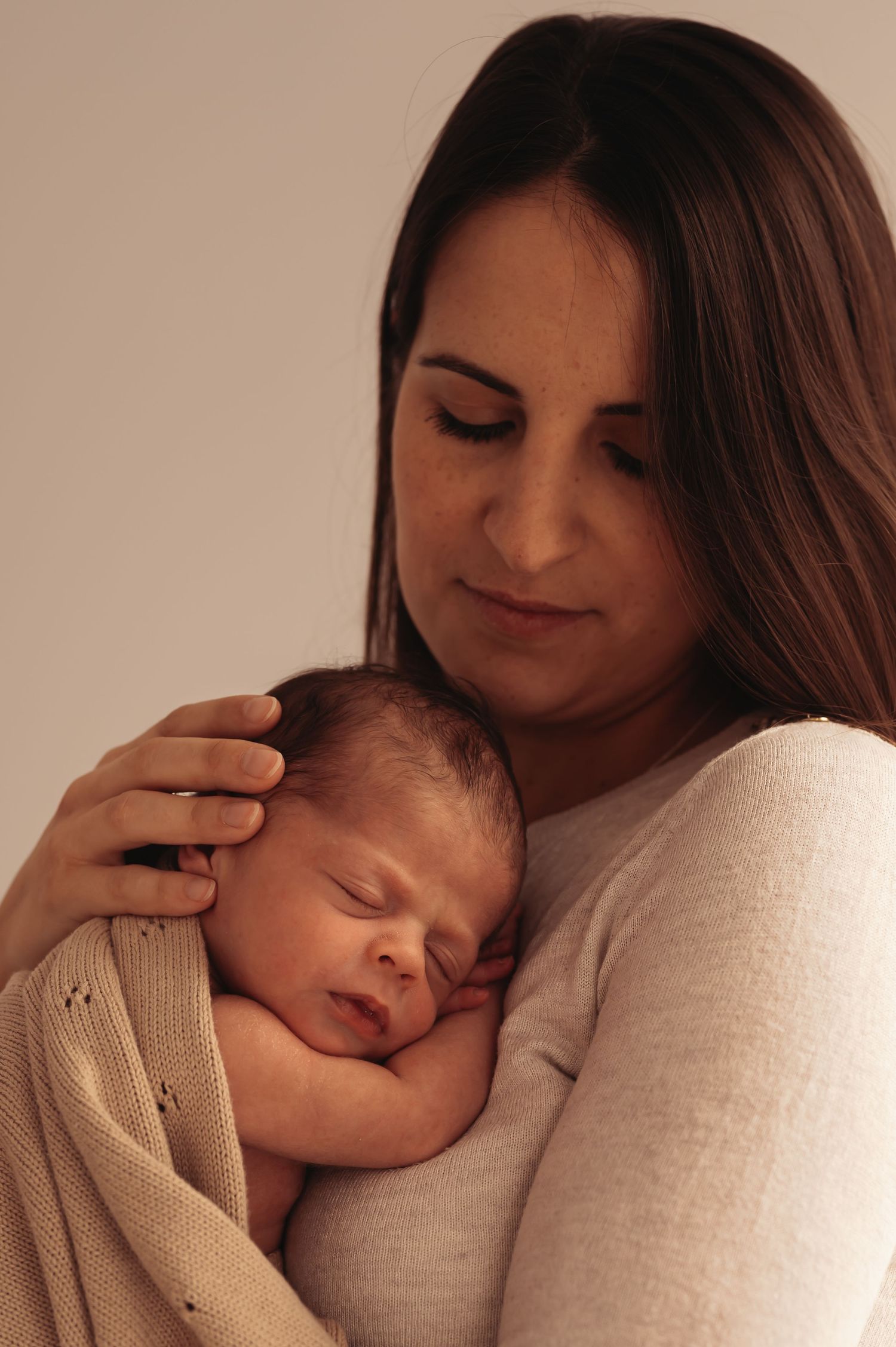 Tender moment between mother and newborn baby wrapped in beige blanket.