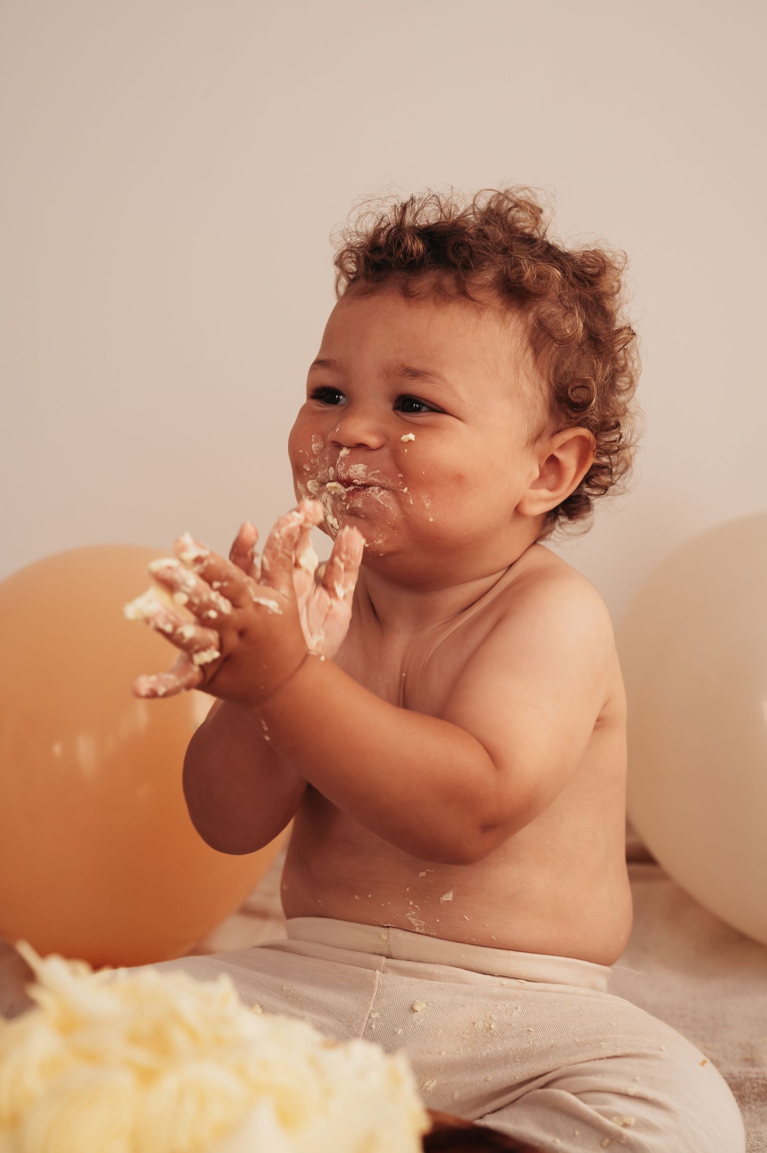 Toddler gleefully eating birthday cake with messy hands during photo session.