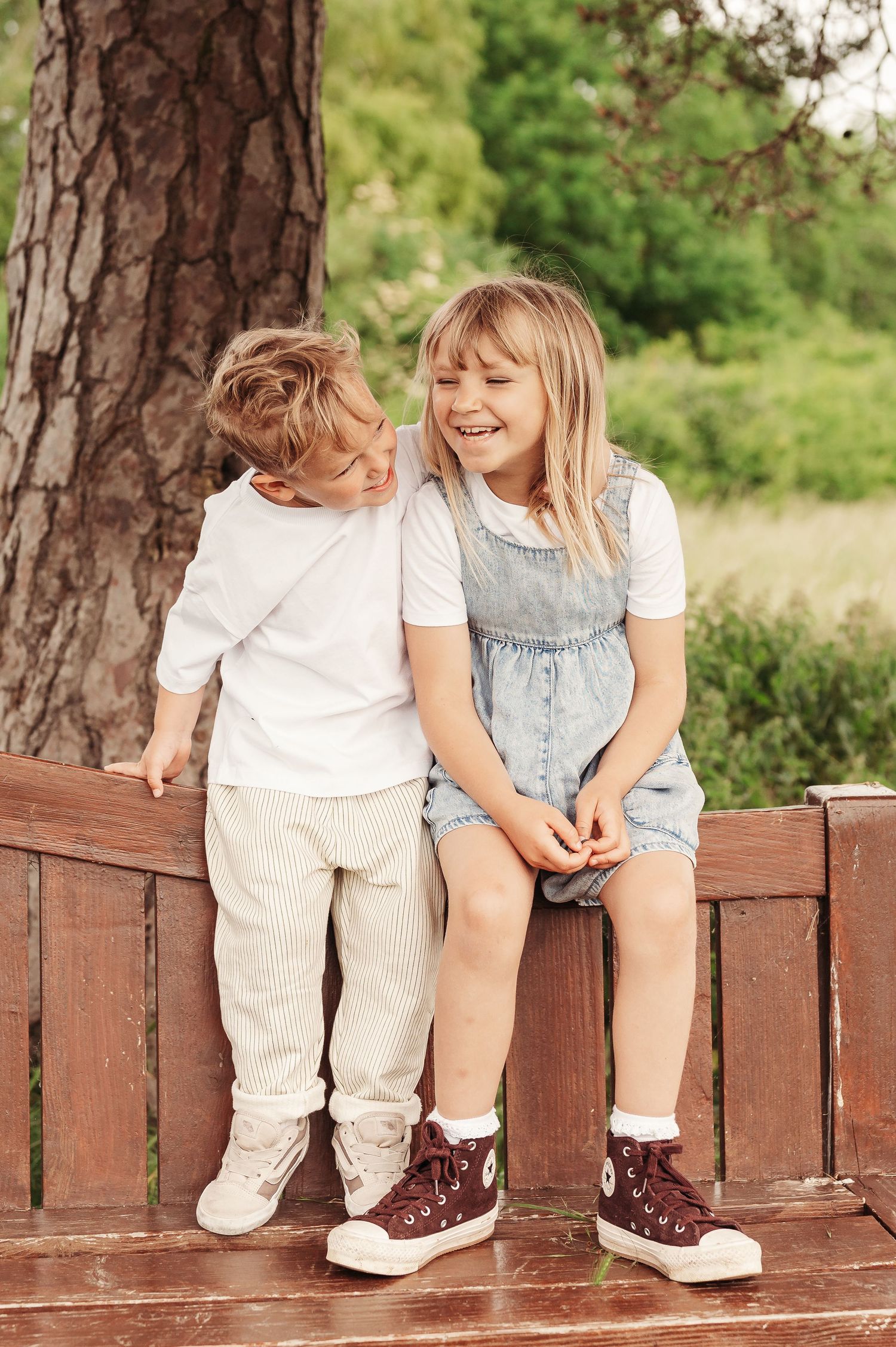 Kids sitting together on a wooden fence sharing a lighthearted moment, wearing casual summer clothes.