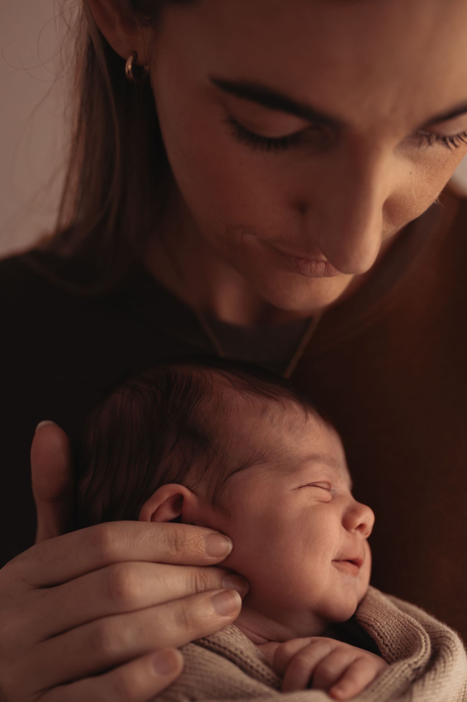 Tender moment between parent and sleeping newborn in warm moody lighting.