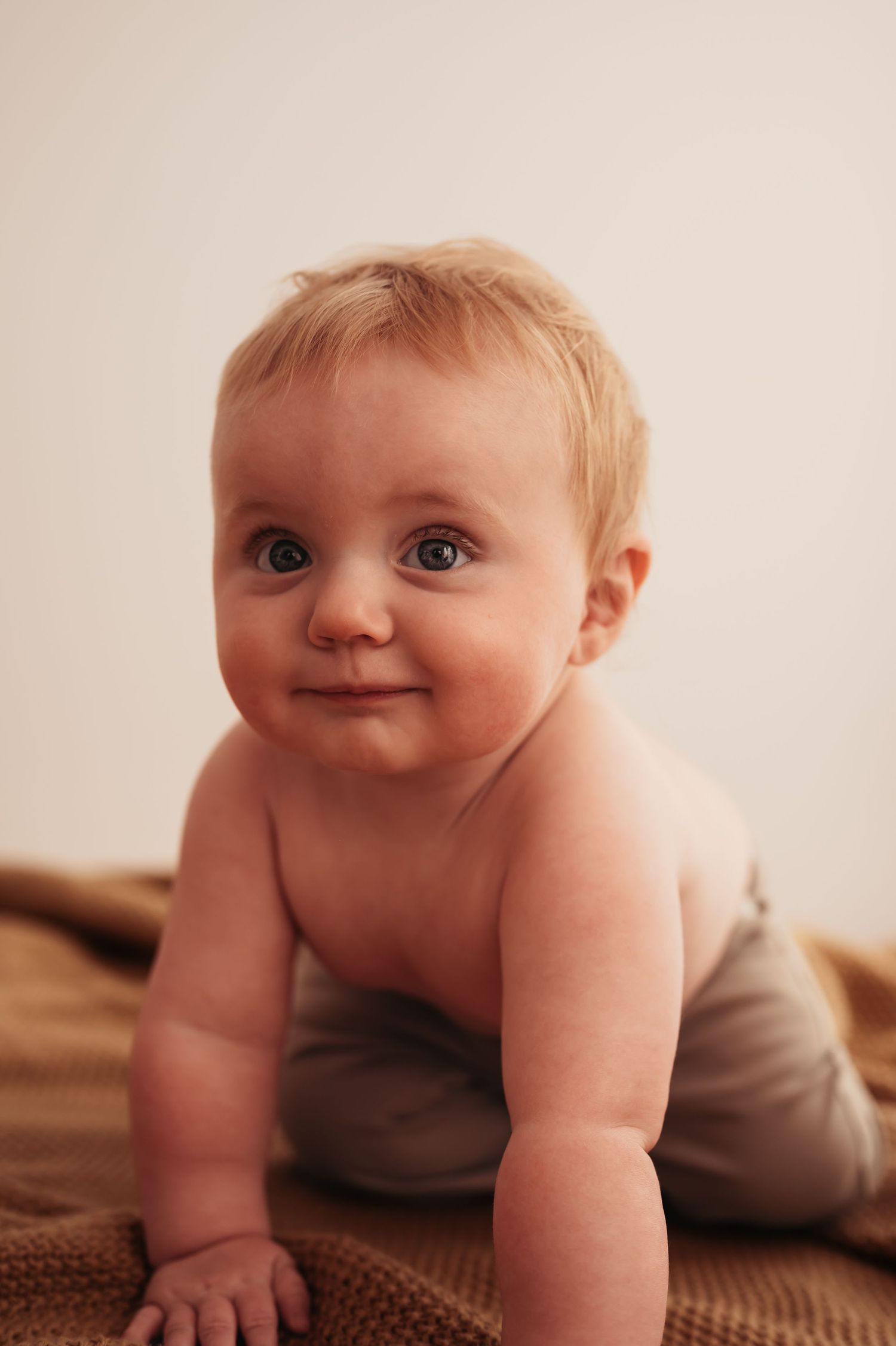 Joyful baby crawling on brown knit blanket with bright eyes and sweet expression.