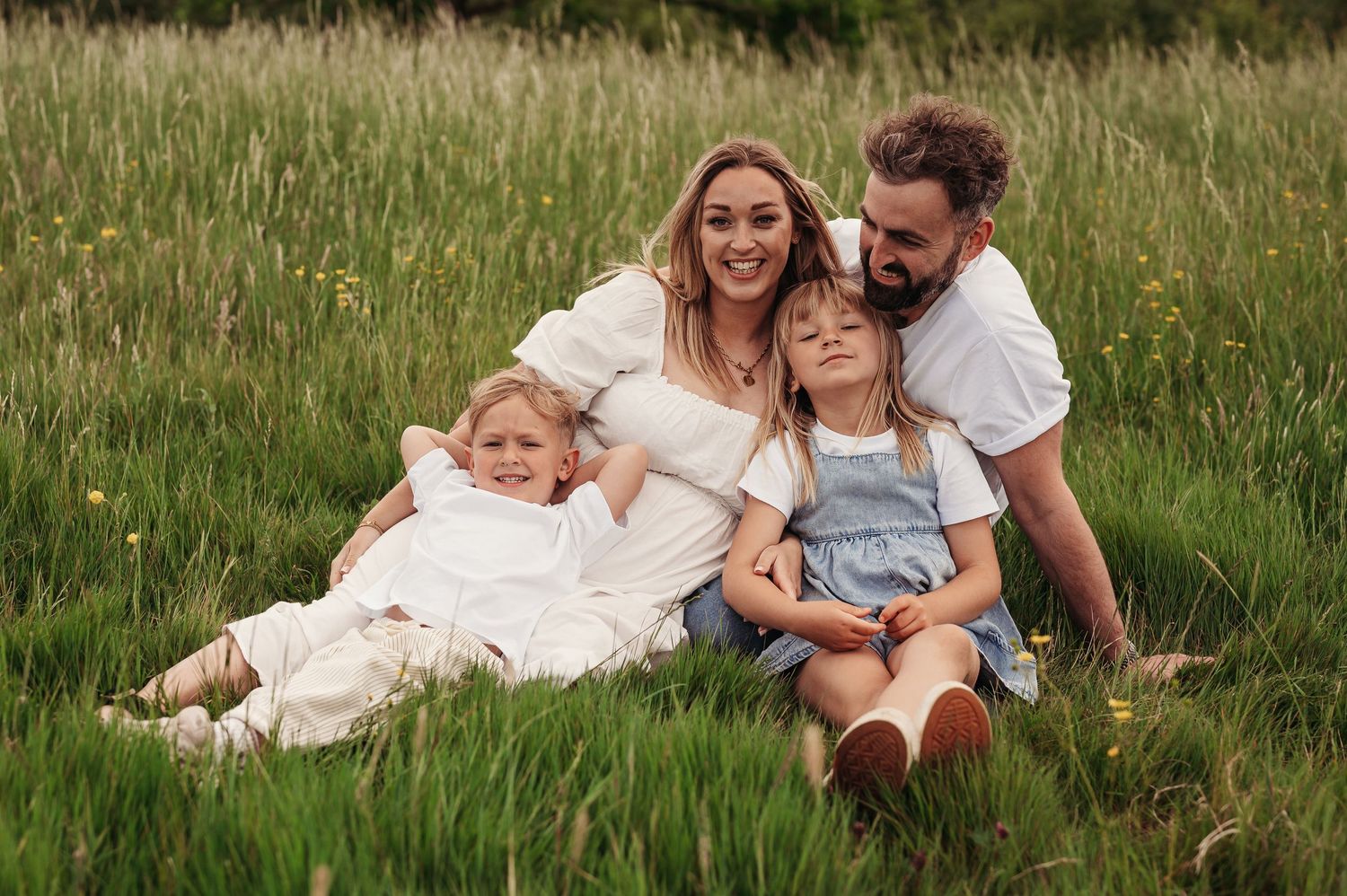A family relaxes together in a grassy meadow during a casual outdoor photoshoot at golden hour.