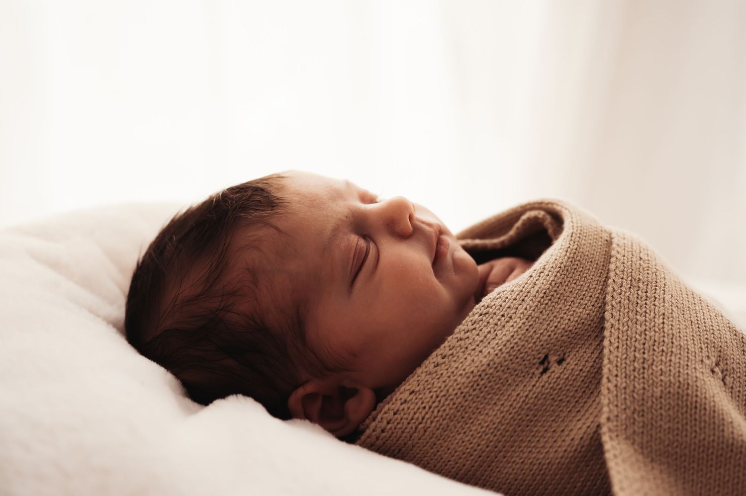 Sleeping newborn baby swaddled in knit blanket resting peacefully on white bedding.