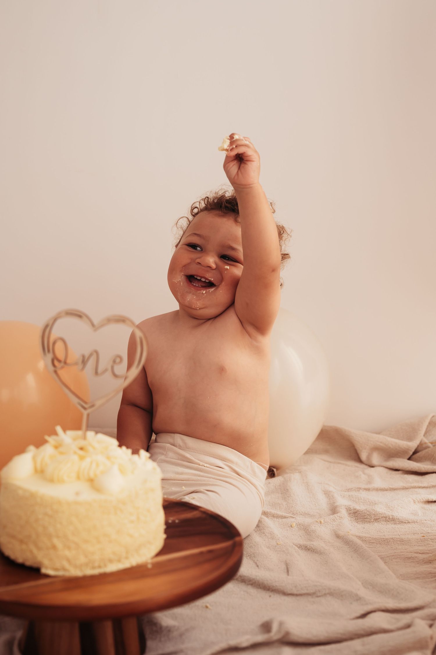 A joyful baby celebrating with a yellow birthday cake and decorative heart topper.