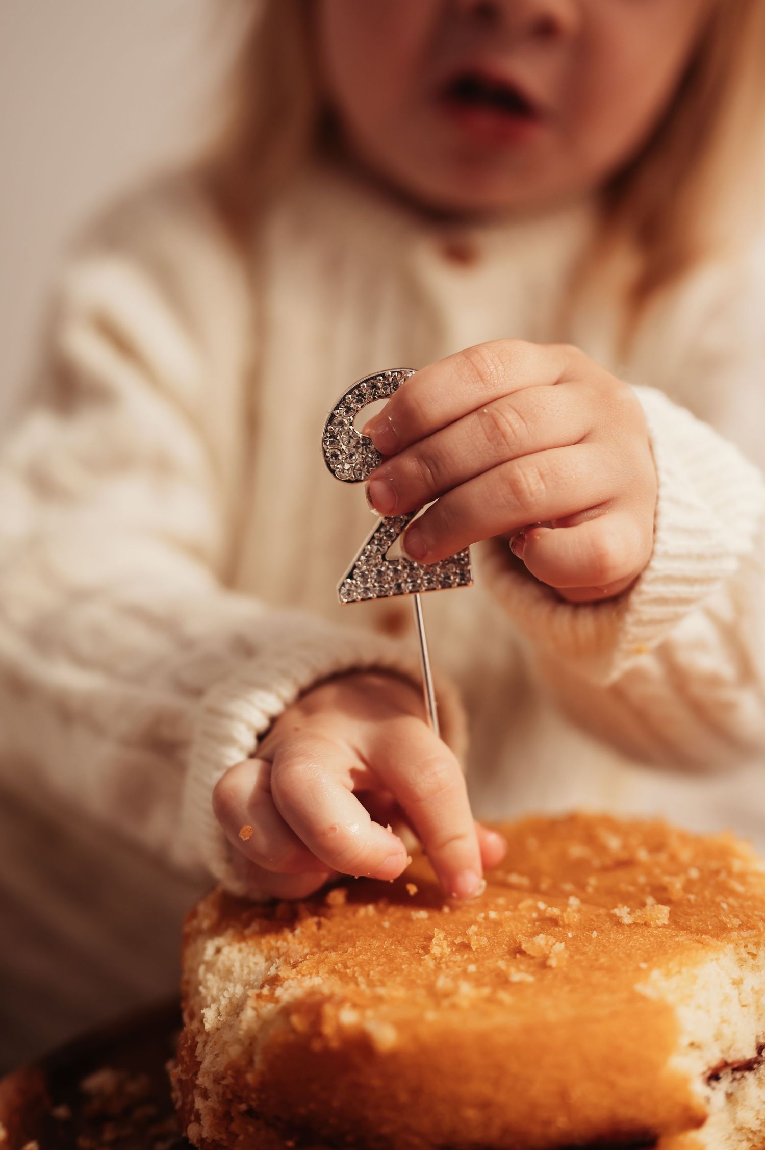 Small hands holding a sparkly number 2 cake topper over a golden cake.