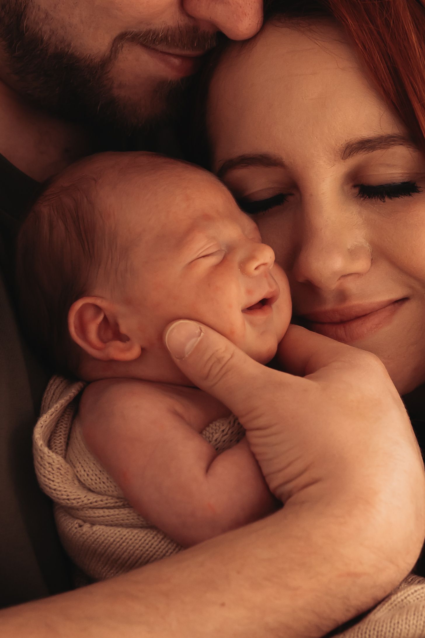 Intimate family moment with sleeping newborn wrapped in knit blanket.
