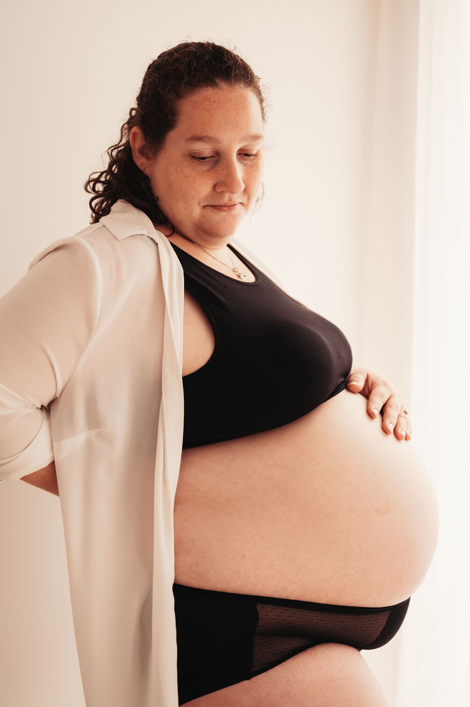 Artistic maternity photo capturing late-stage pregnancy in natural window light.