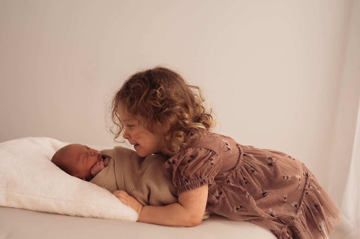 Tender moment between siblings on white bedding with beige blanket.