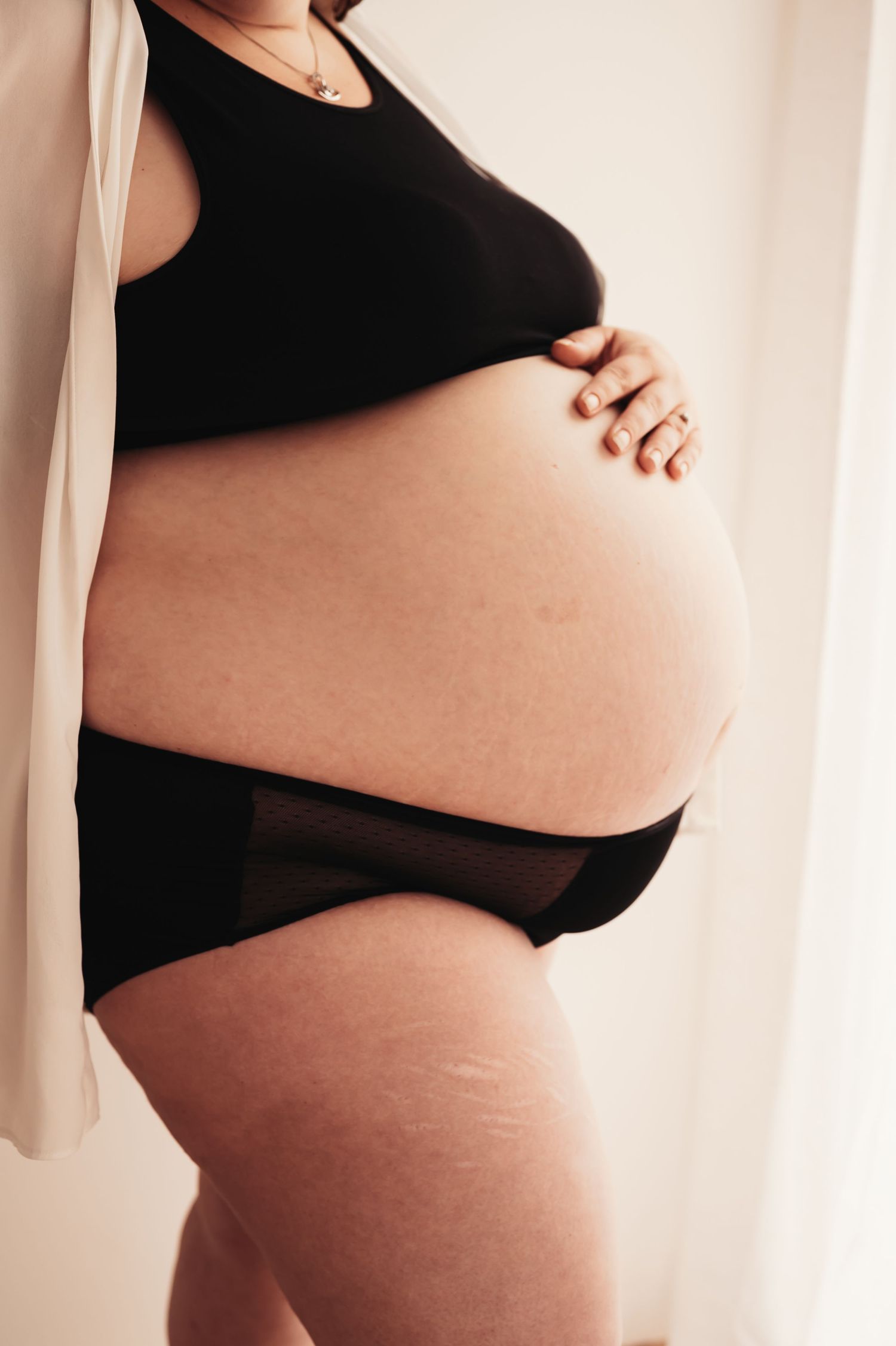 Side view of pregnant belly in black maternity wear against neutral background.