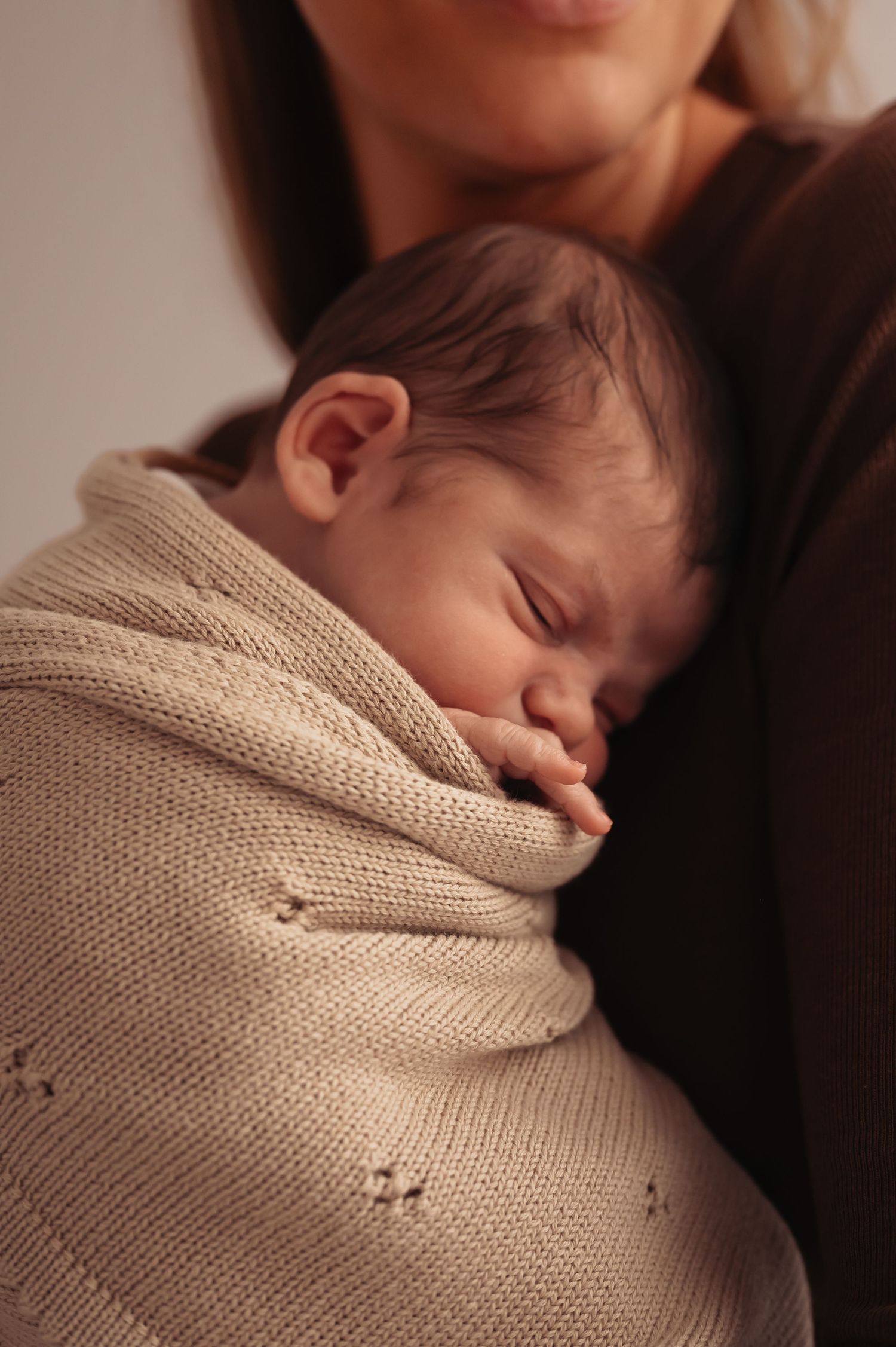 Close-up of sleeping baby in patterned beige wrap being held lovingly.