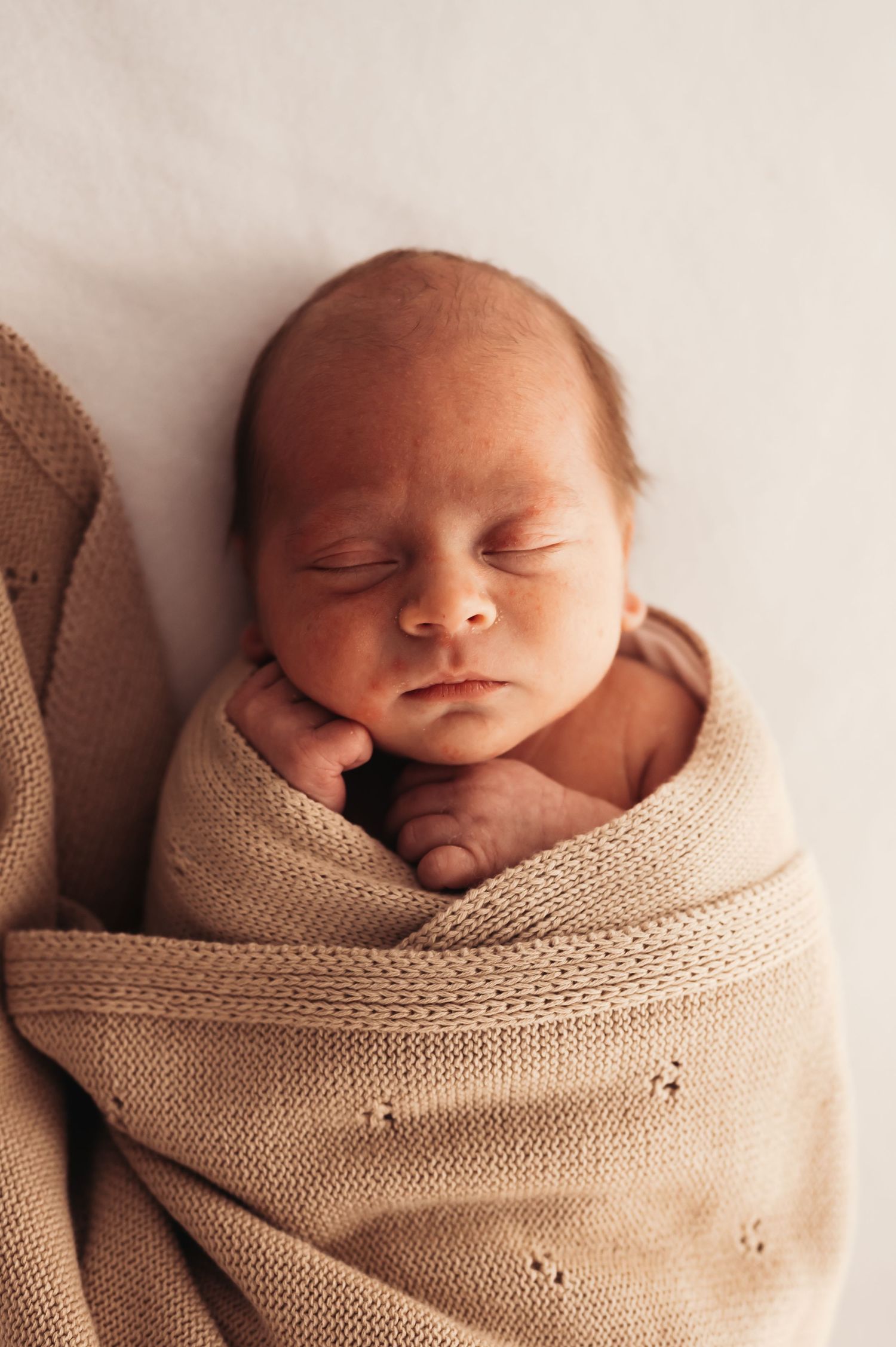 Newborn nestled in soft beige knitted wrap during professional photoshoot.