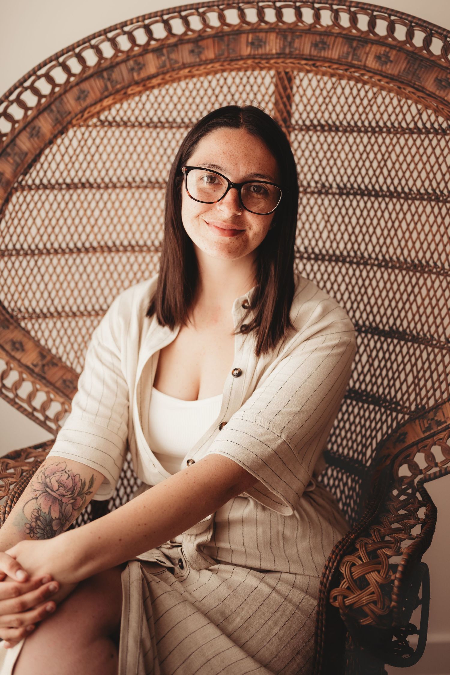 A self-portrait of owner in glasses and cardigan sits on a decorative wicker peacock chair.