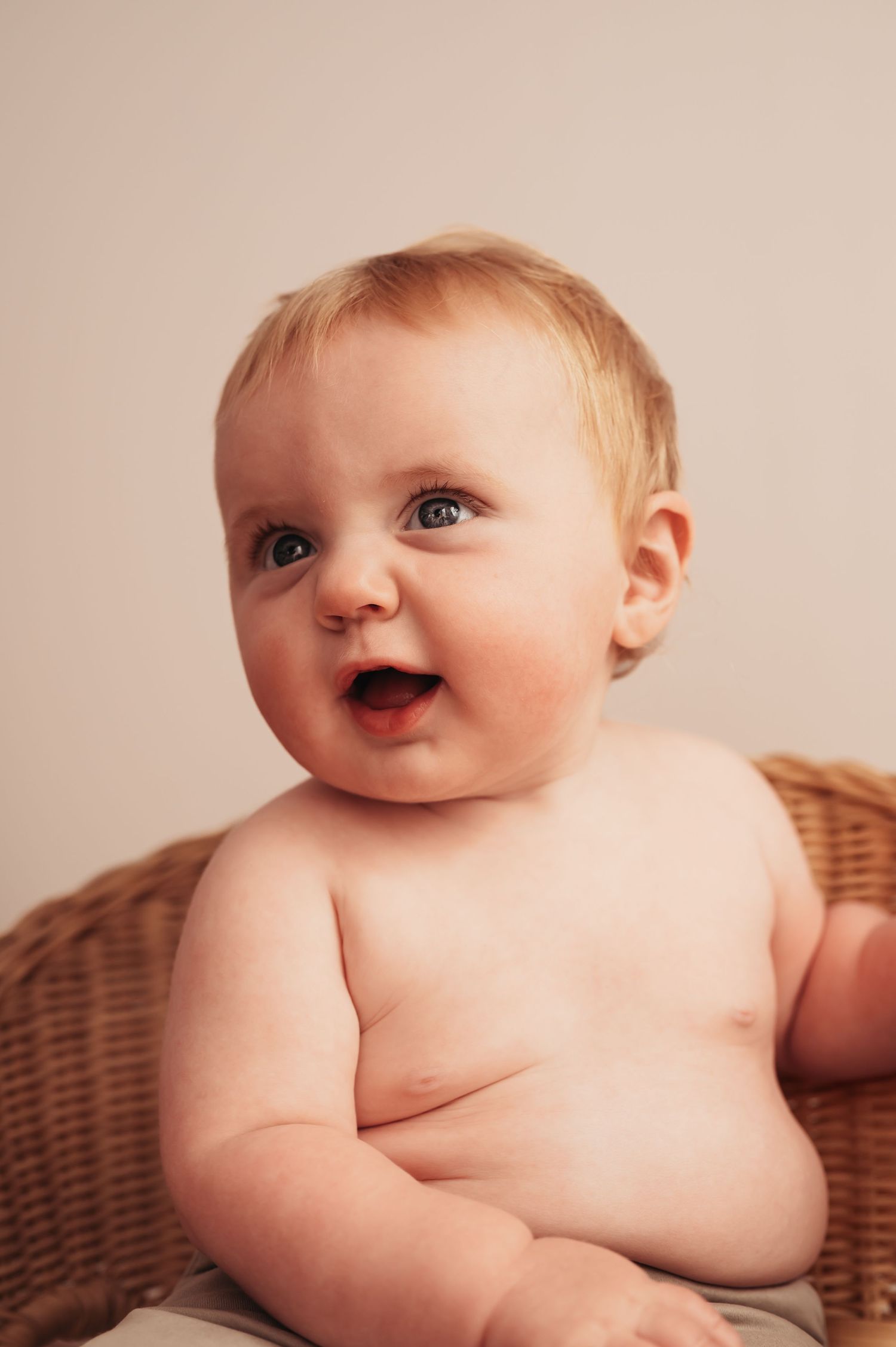 Joyful baby sits in wicker chair during professional photo session.
