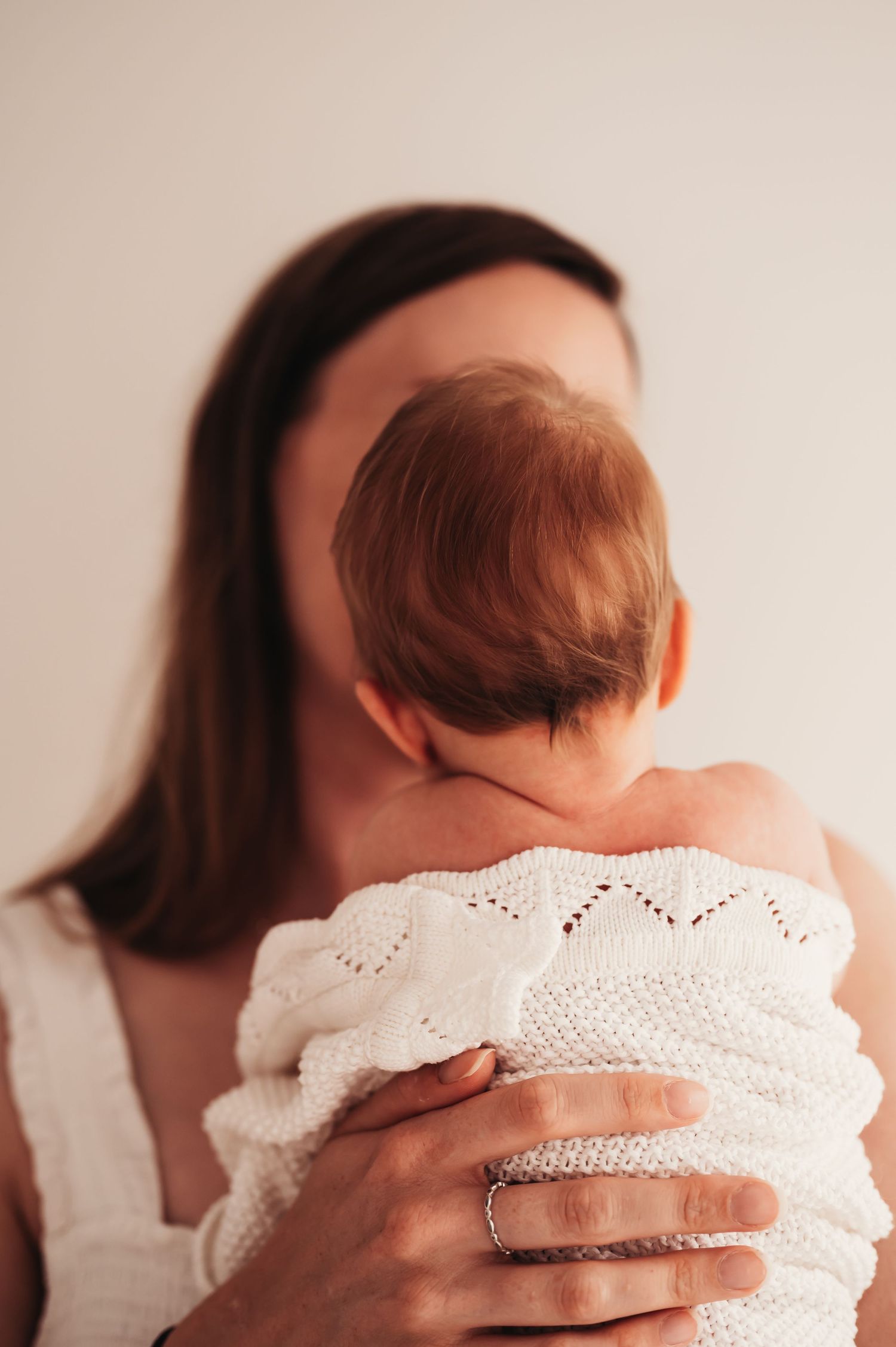 A parent in white lace clothing cradles an infant wrapped in a knit blanket.
