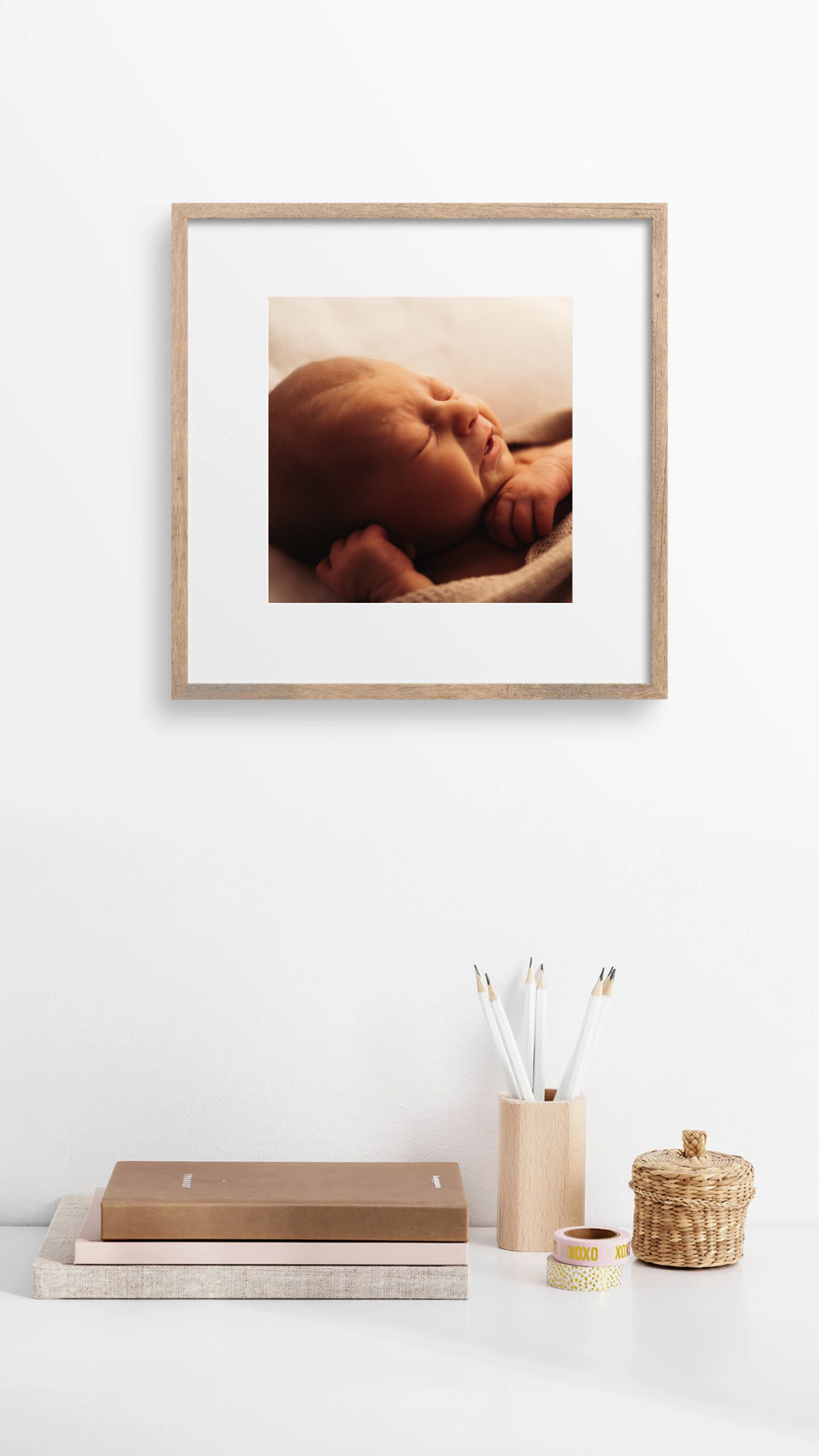 A framed square photo on white wall with minimalist desk accessories below.