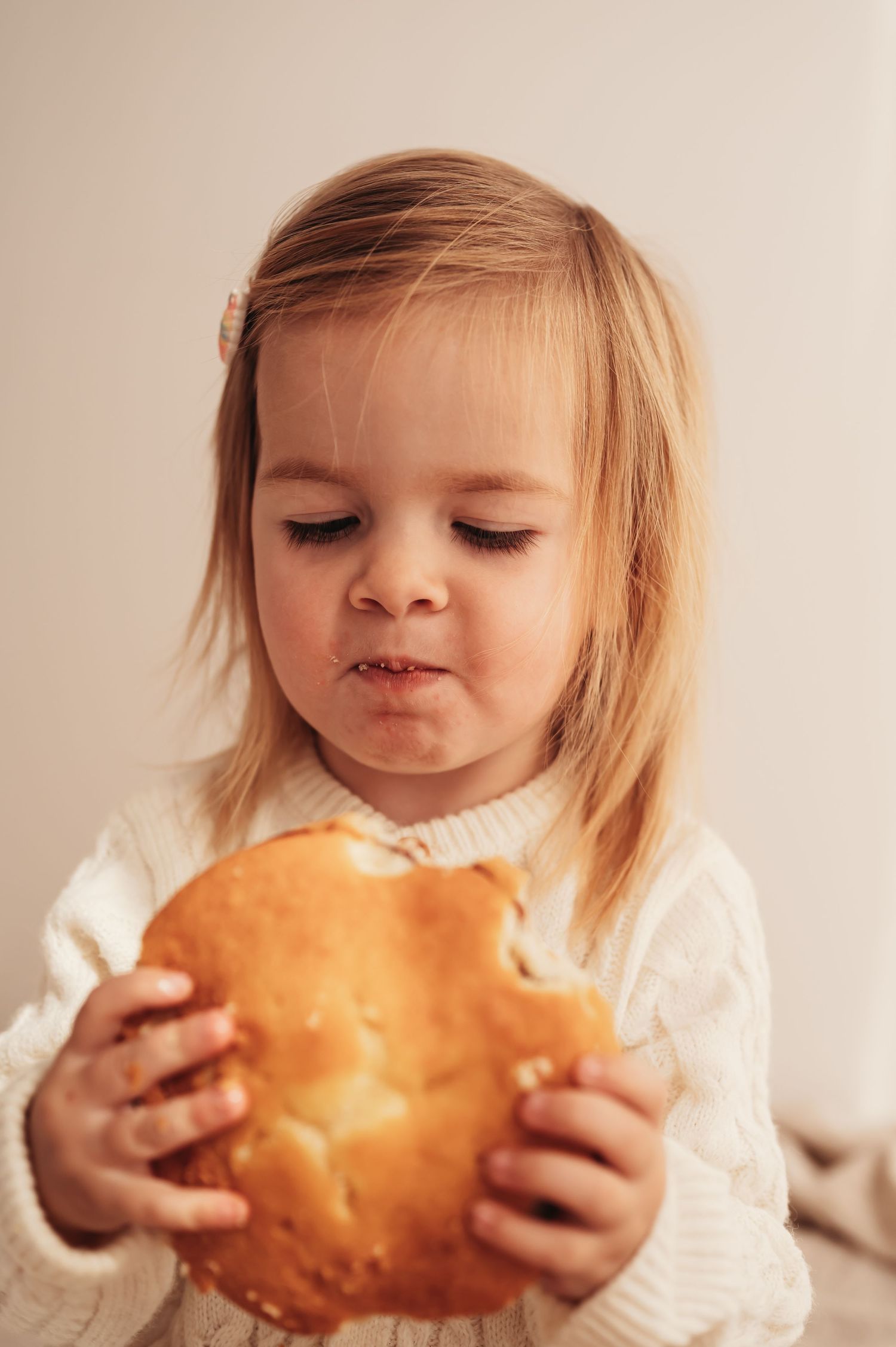 A small child in a white sweater examining a yummy cake with curiosity.