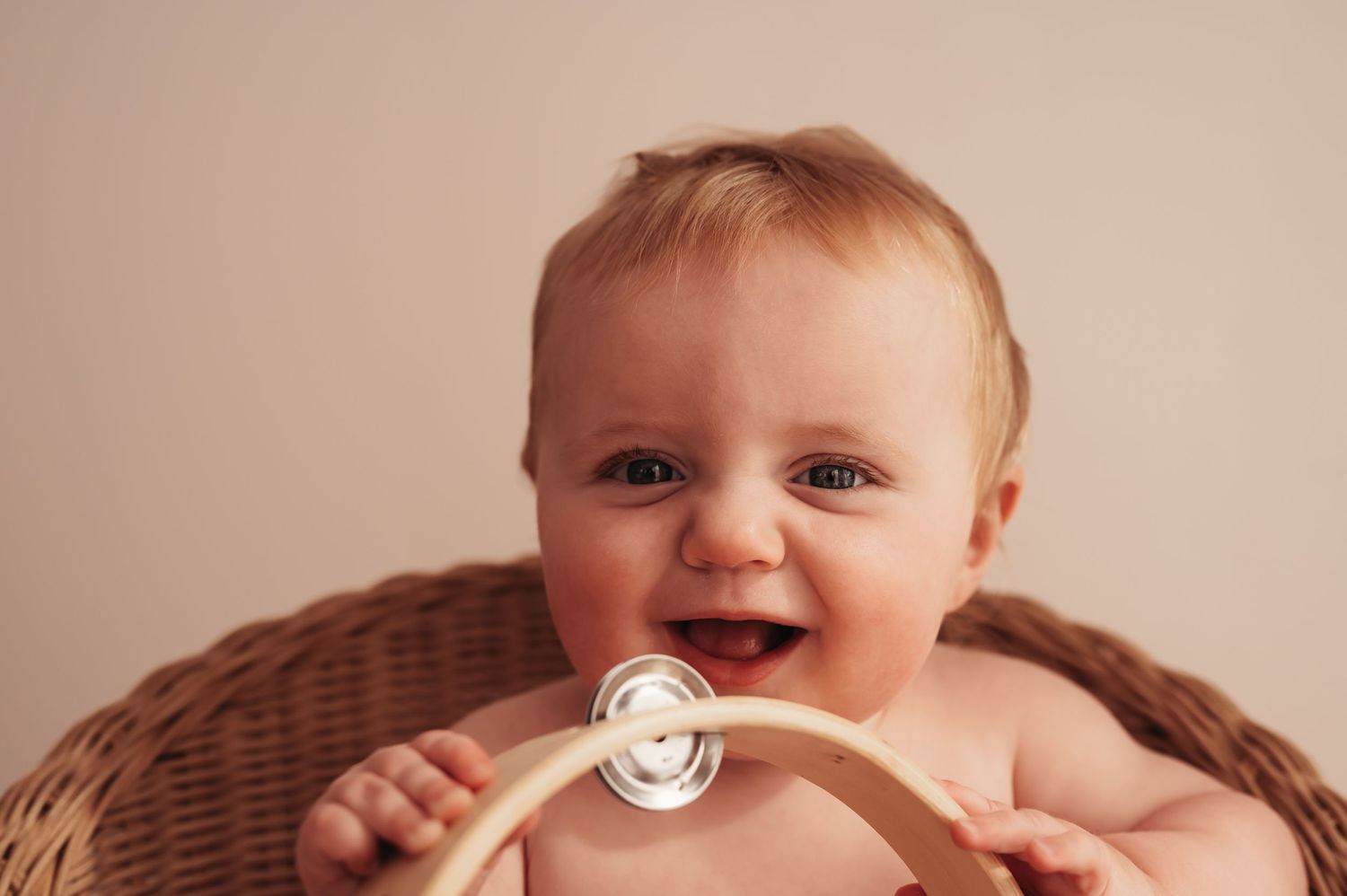 Happy baby playing with wooden toy while sitting in wicker basket.