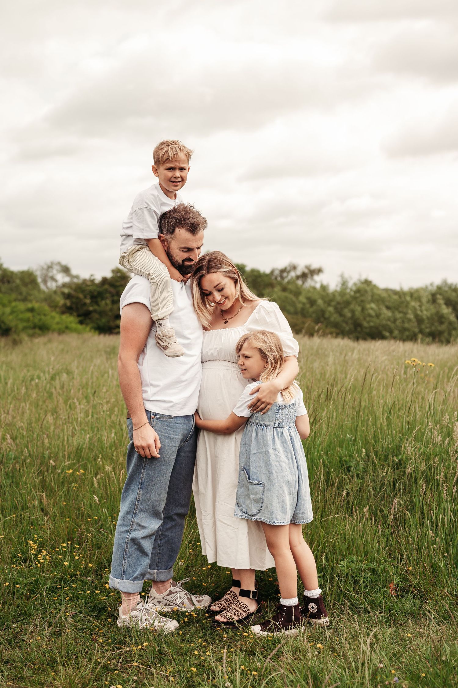Candid family portrait in a grassy meadow shows a group of four embracing during golden hour.