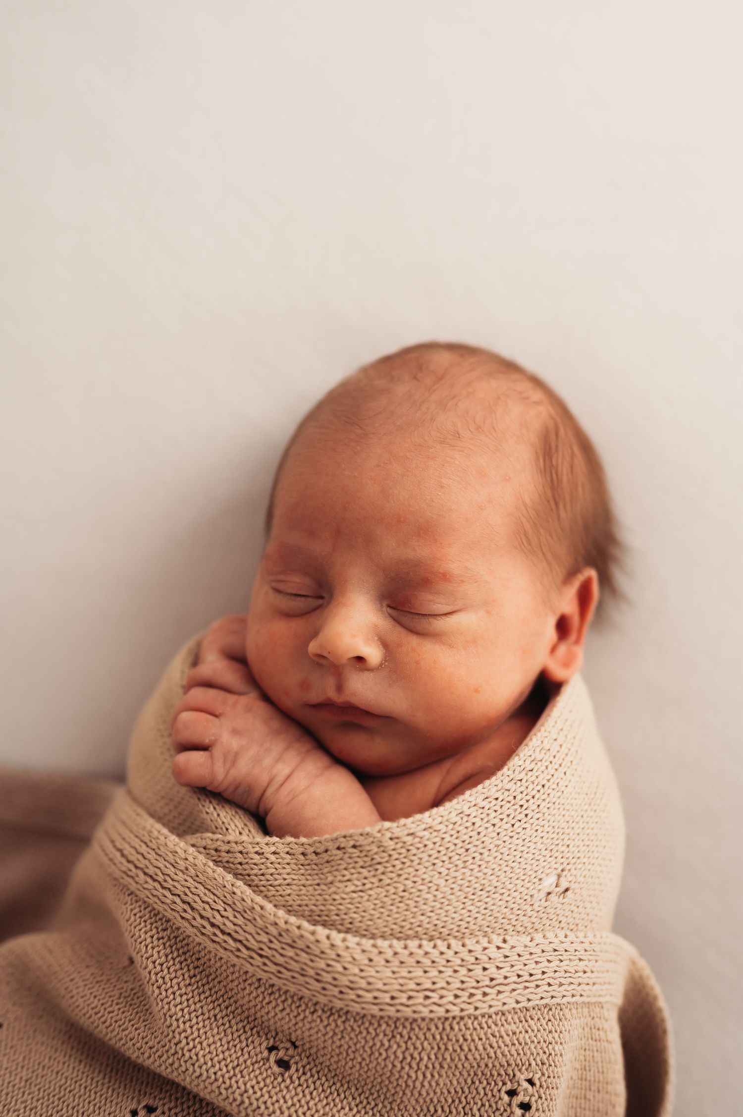 Newborn baby peacefully sleeping while wrapped in soft beige knitted blanket.