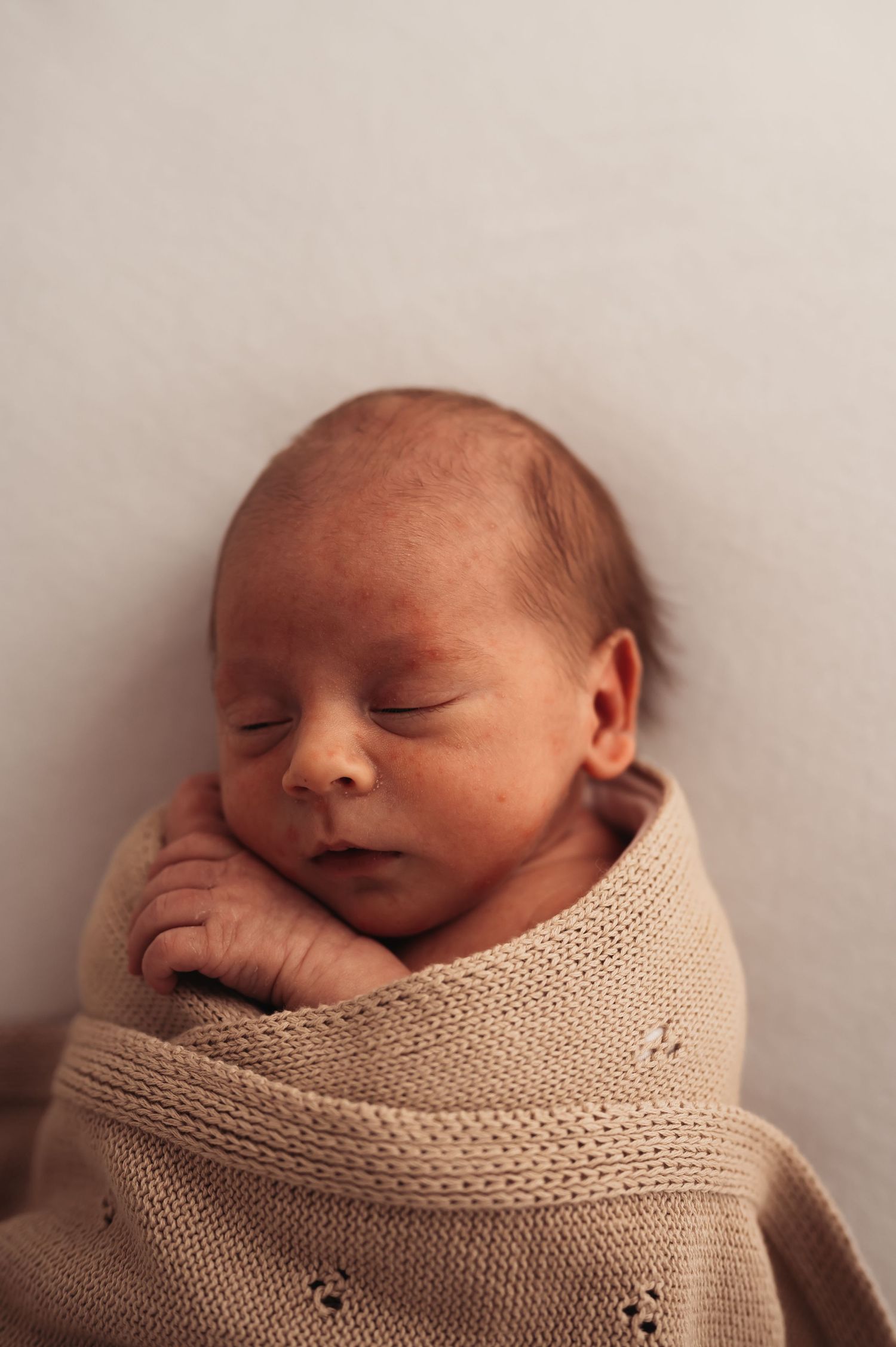 Peaceful newborn baby sleeping while swaddled in soft beige knitted blanket with delicate floral pattern.
