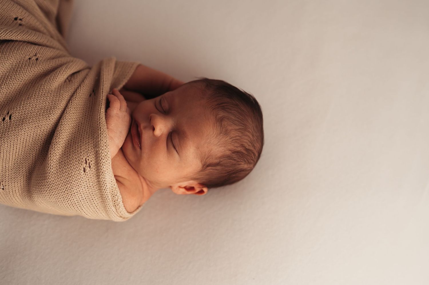 Sleeping newborn wrapped in textured beige blanket against white background.
