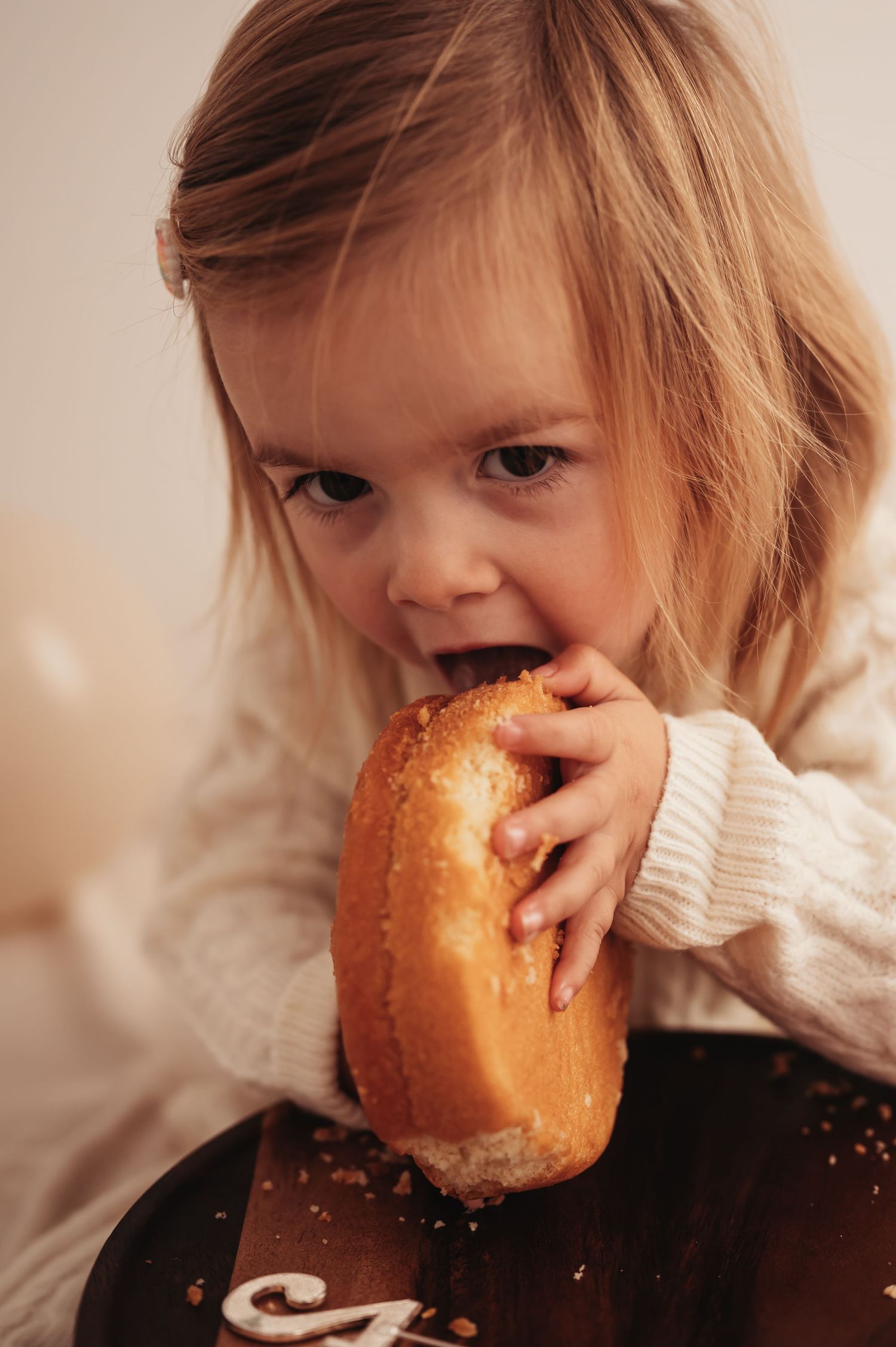 Young person taking big bite of donut while wearing cream sweater.