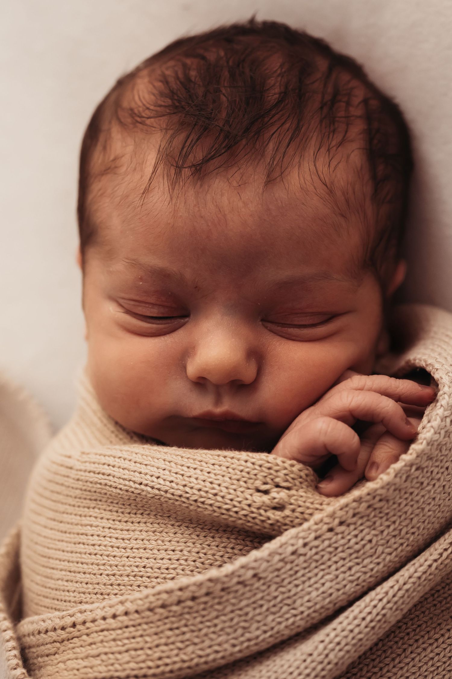 Newborn baby napping peacefully in soft knitted beige wrap.